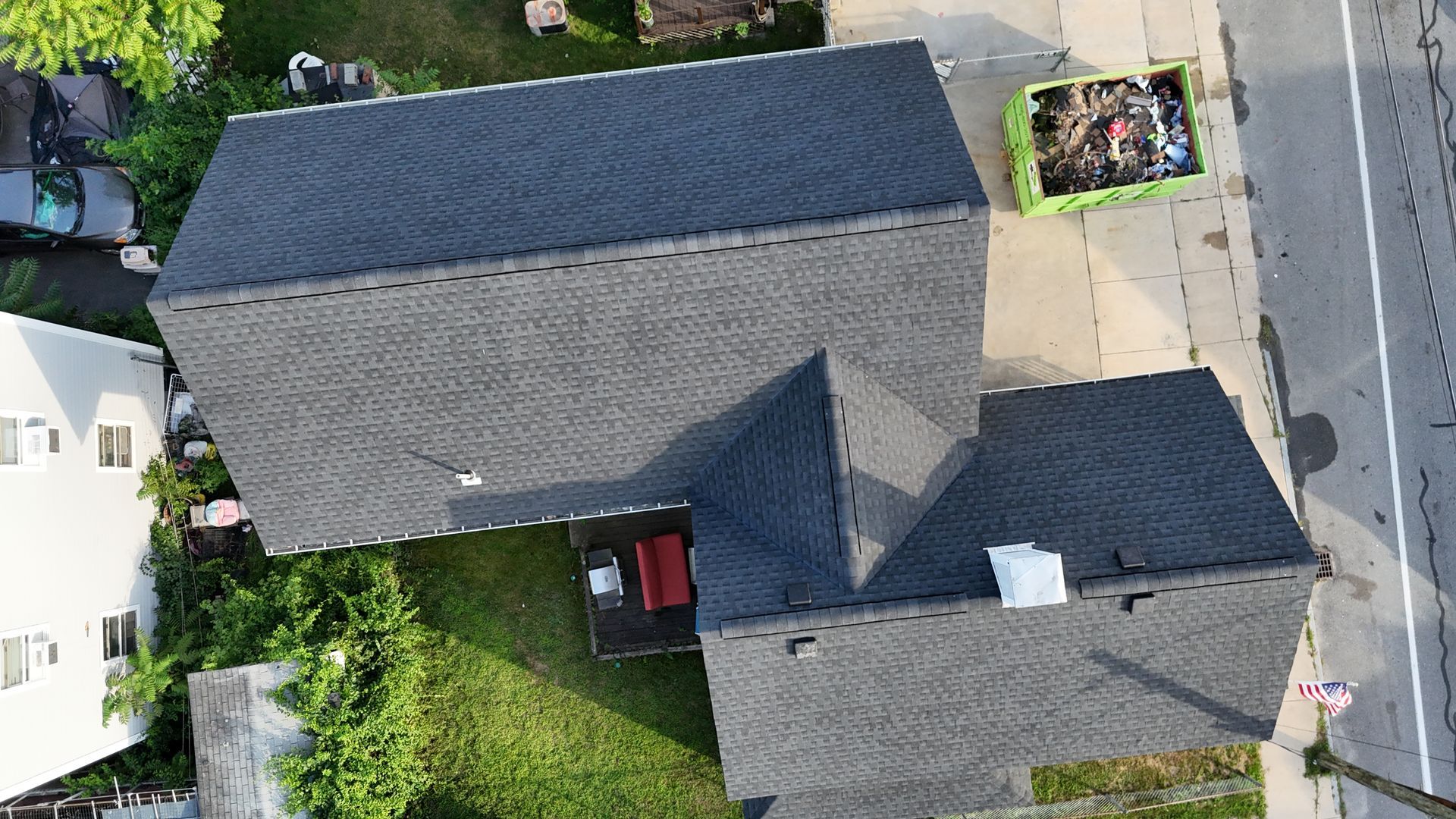 Aerial view of a gray-roofed house with driveway, yard, and parked car beside a street