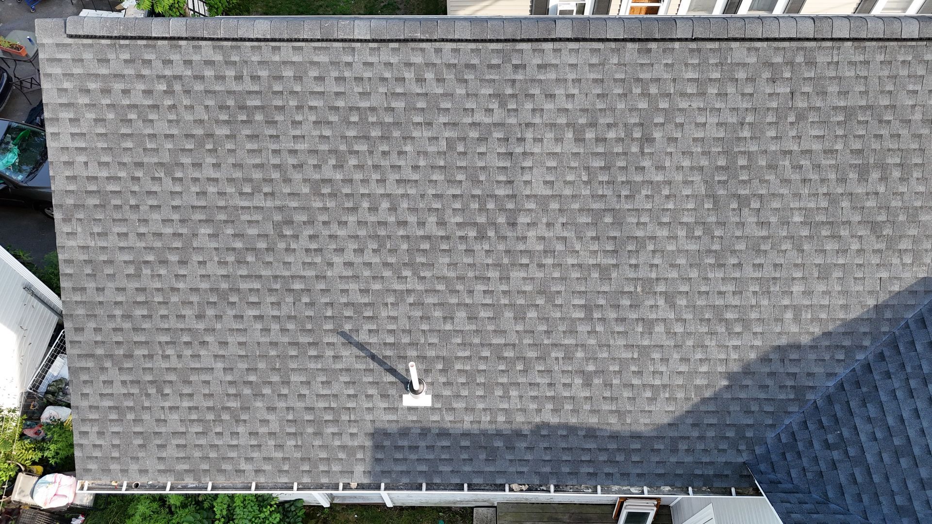 Aerial view of a gray shingled roof with a small white vent and a shadow across the right side