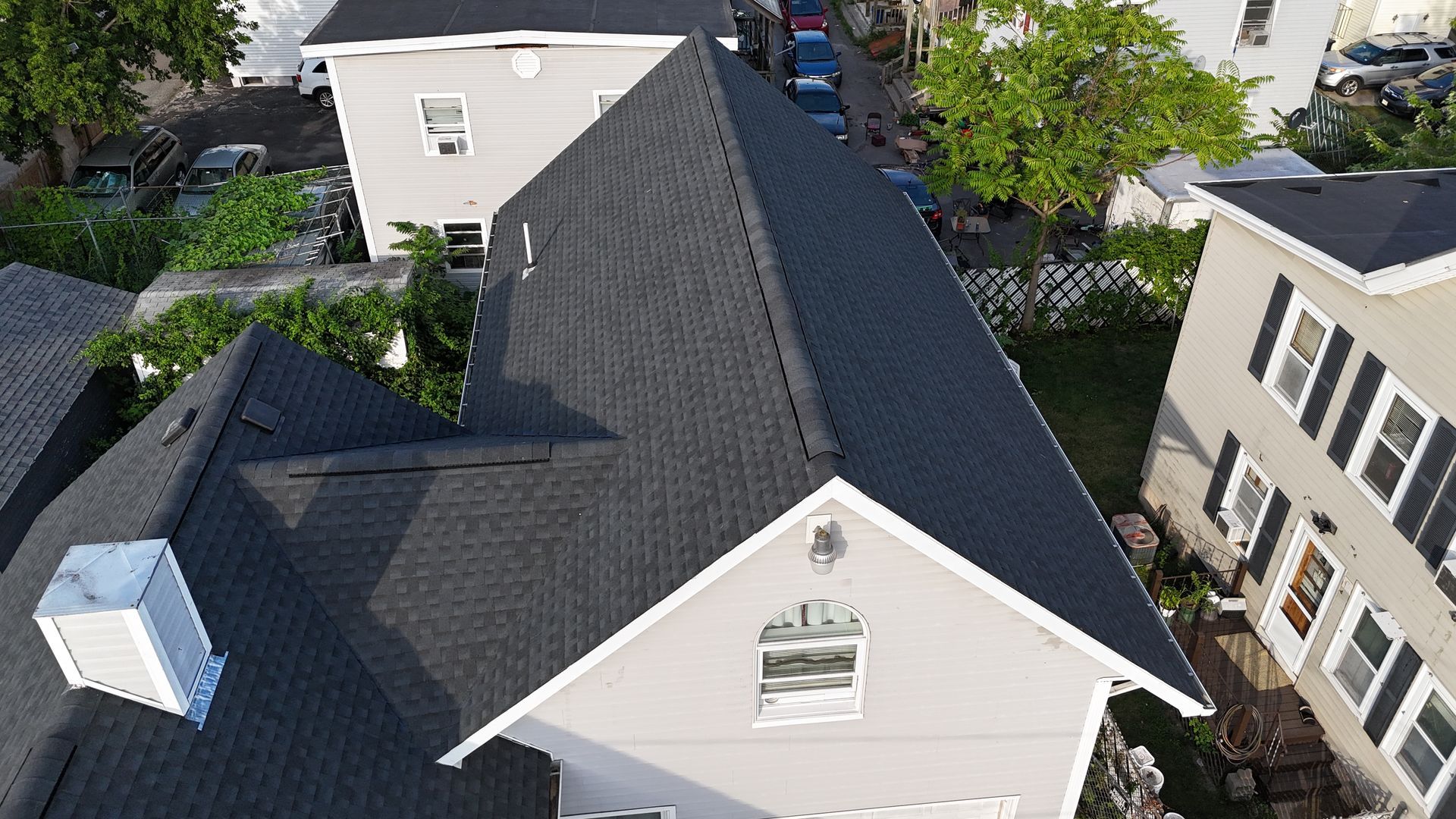 Aerial view of a gray-roofed house with beige siding among neighboring homes and trees