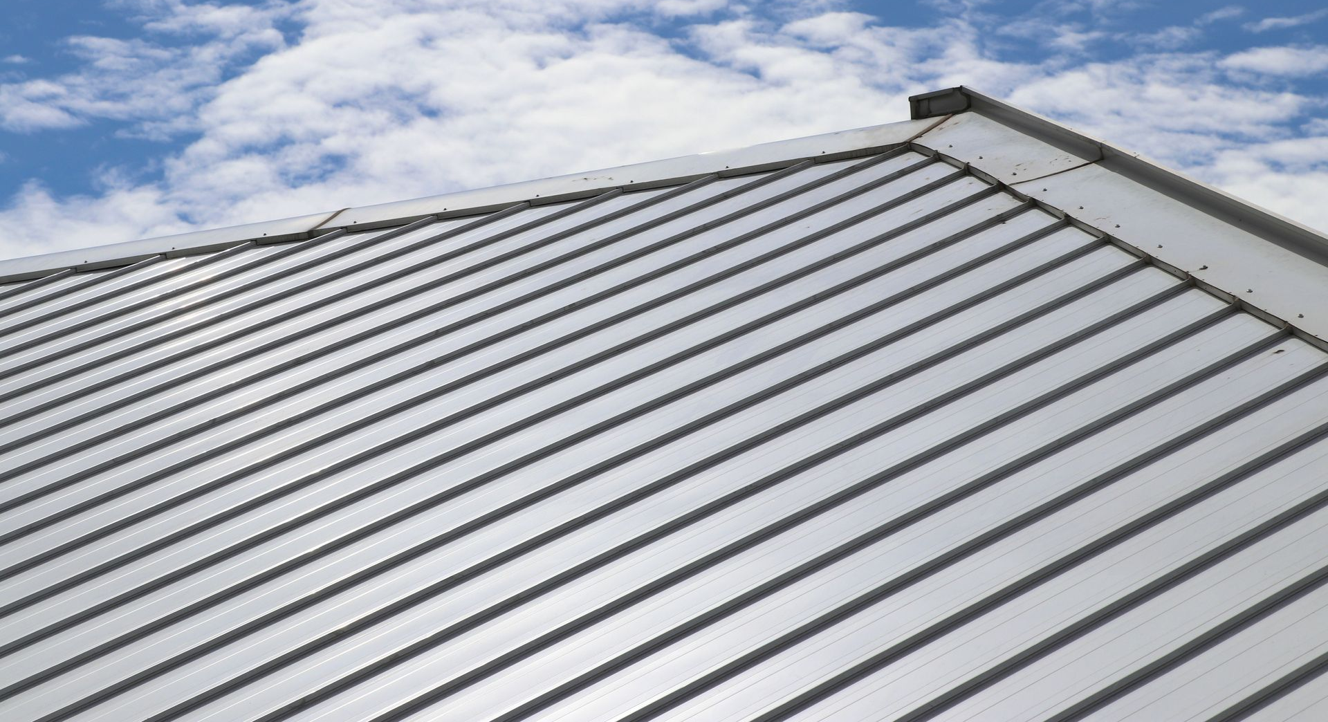 Metal roof with gray standing seams beneath a partly cloudy blue sky