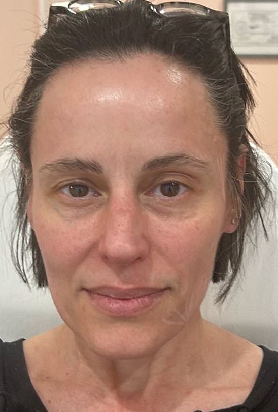 A front-facing headshot of a person with dark hair, glasses on their head, and a neutral expression.