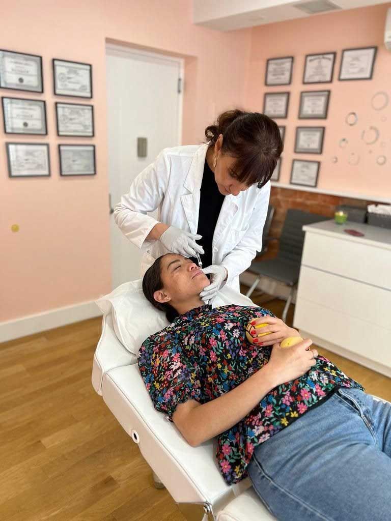 Woman in a lab coat giving a facial treatment to a person lying down in a spa.