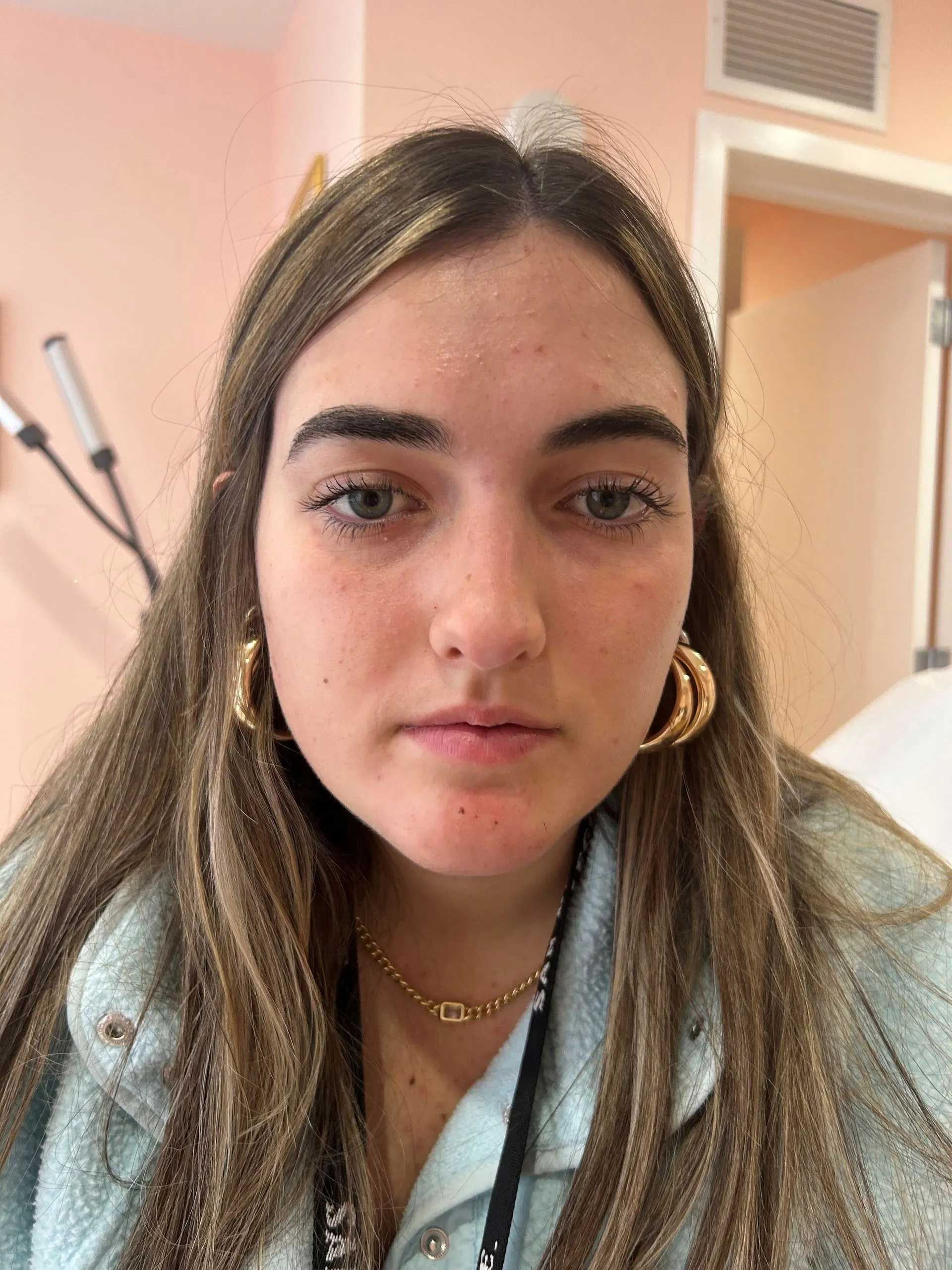 Woman with long brown hair wearing gold hoop earrings and a light blue jacket.