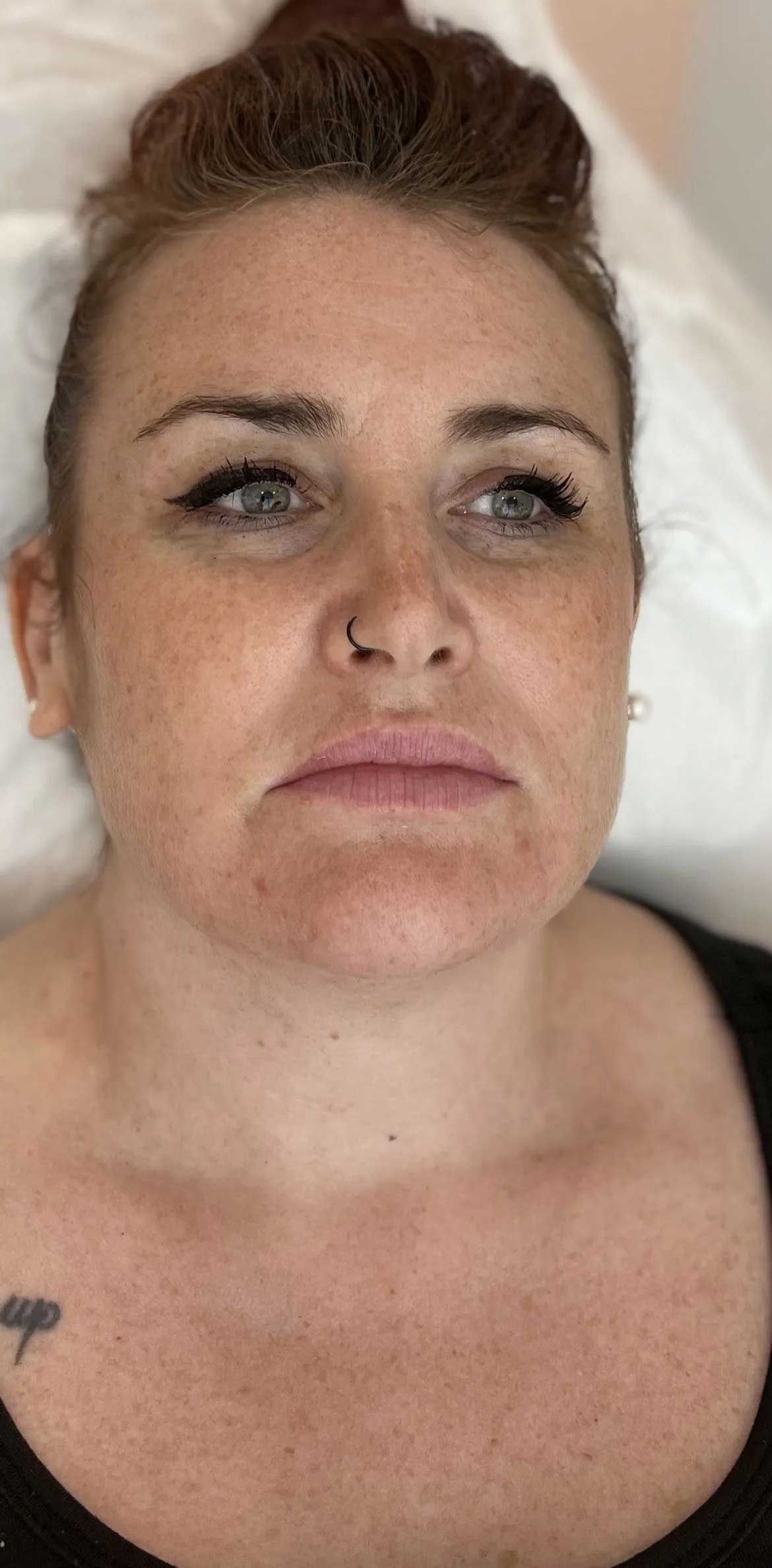 Woman with red hair pulled up, freckled skin, and a small tattoo on her shoulder.