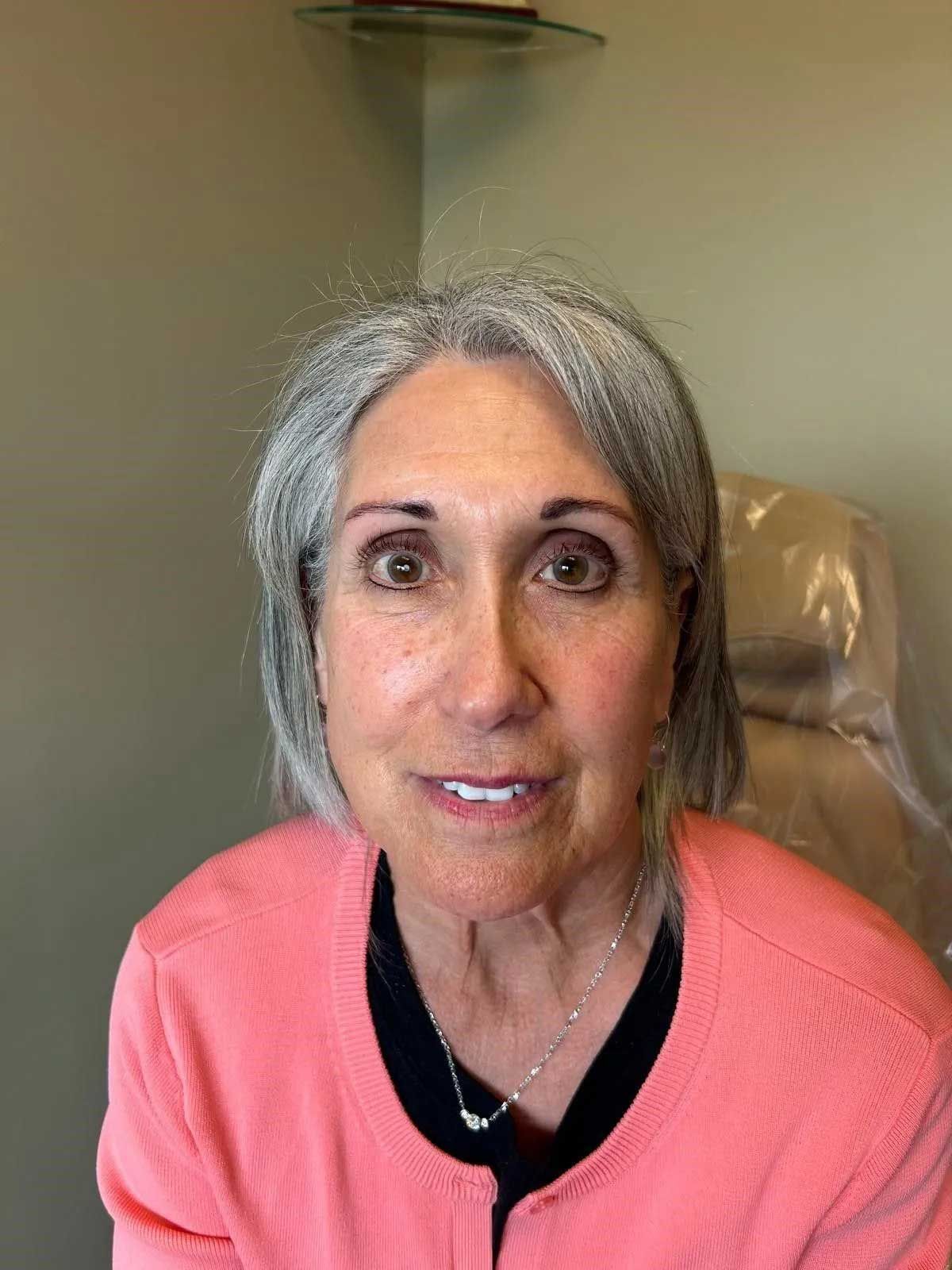 Woman with gray hair and a pink sweater smiles in a dental office.