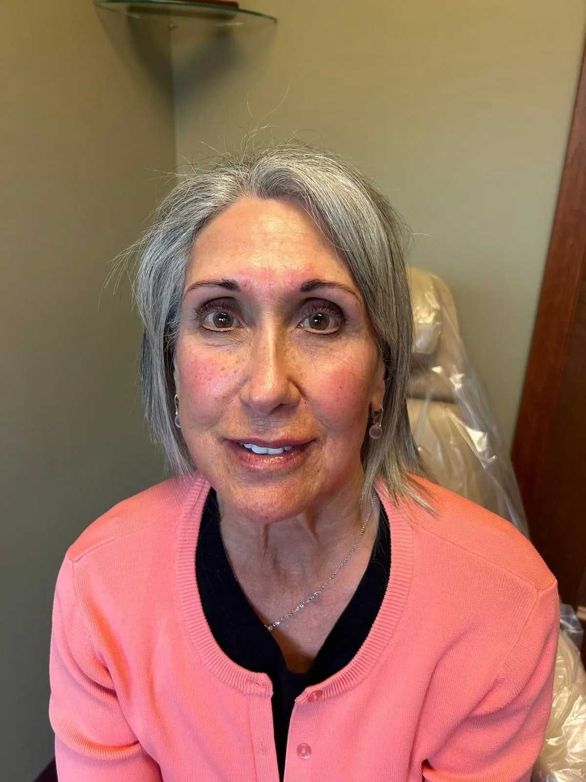 Woman with grey hair, wearing a pink sweater, smiling at the camera.