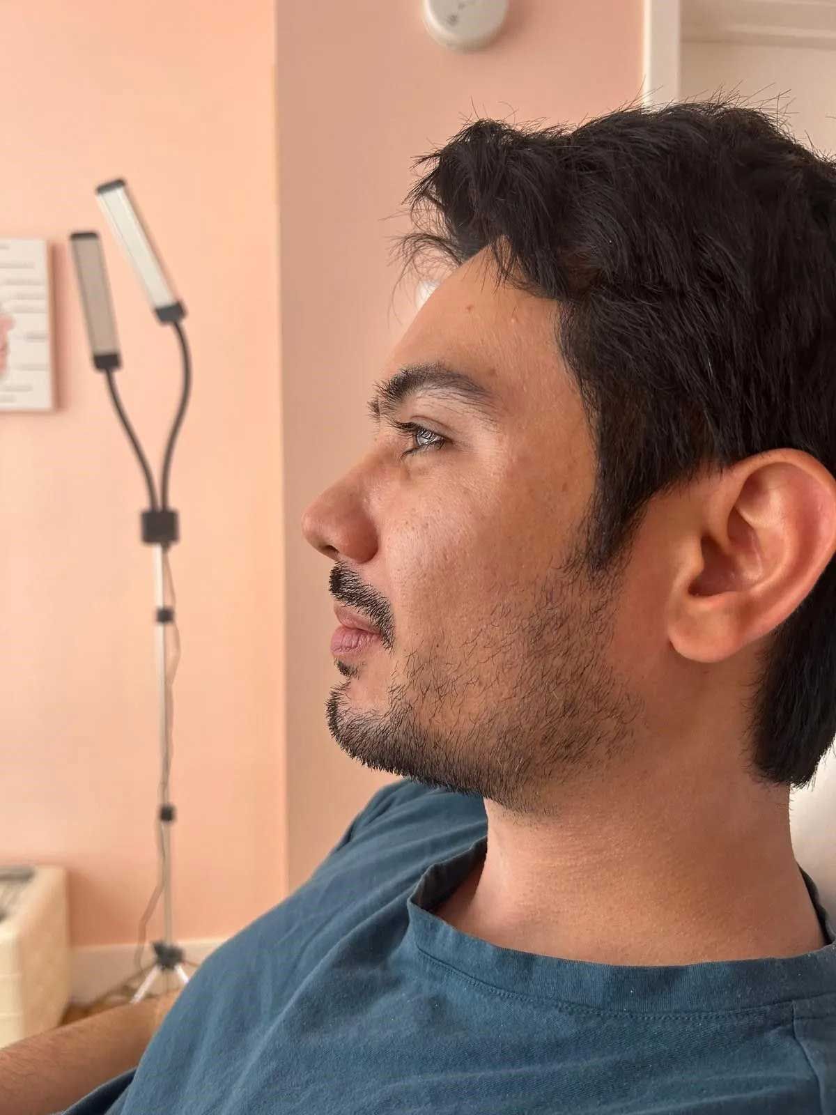 Man with dark hair and facial hair, in a room with a light, looking towards the right.