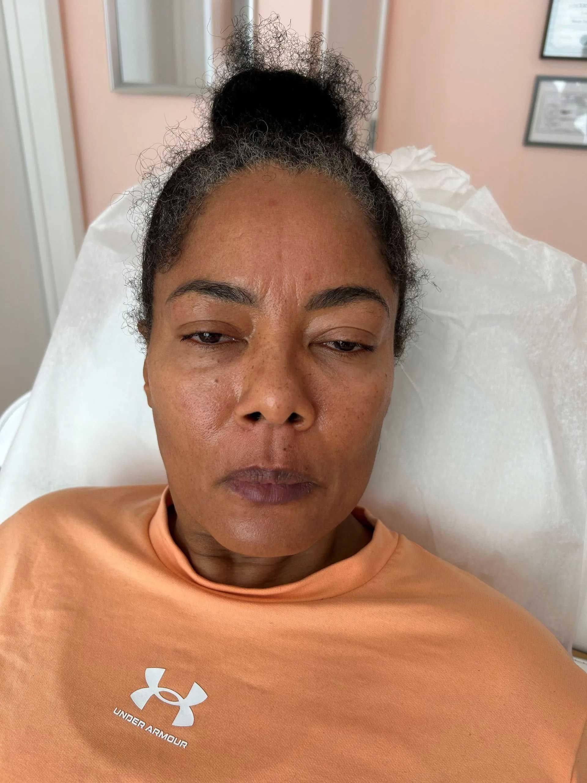 Woman with dark hair in a bun, wearing an orange shirt, seated in a medical setting.