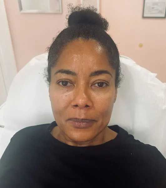 Woman with dark hair in a bun, seated, gazing forward. Wearing a black shirt. Indoor setting.