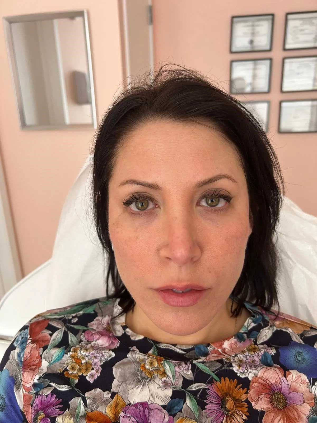 Woman with dark hair in clinic setting, looking at the camera, wearing a floral top.
