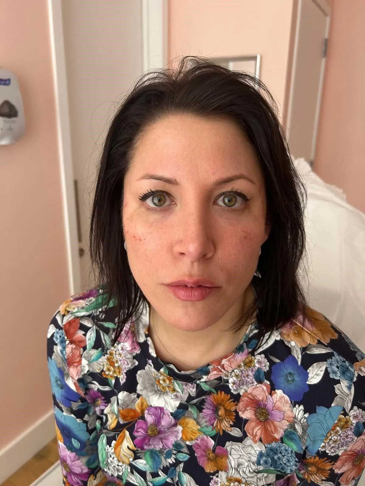 Woman with dark hair and floral shirt; looking forward. Pink-walled room.