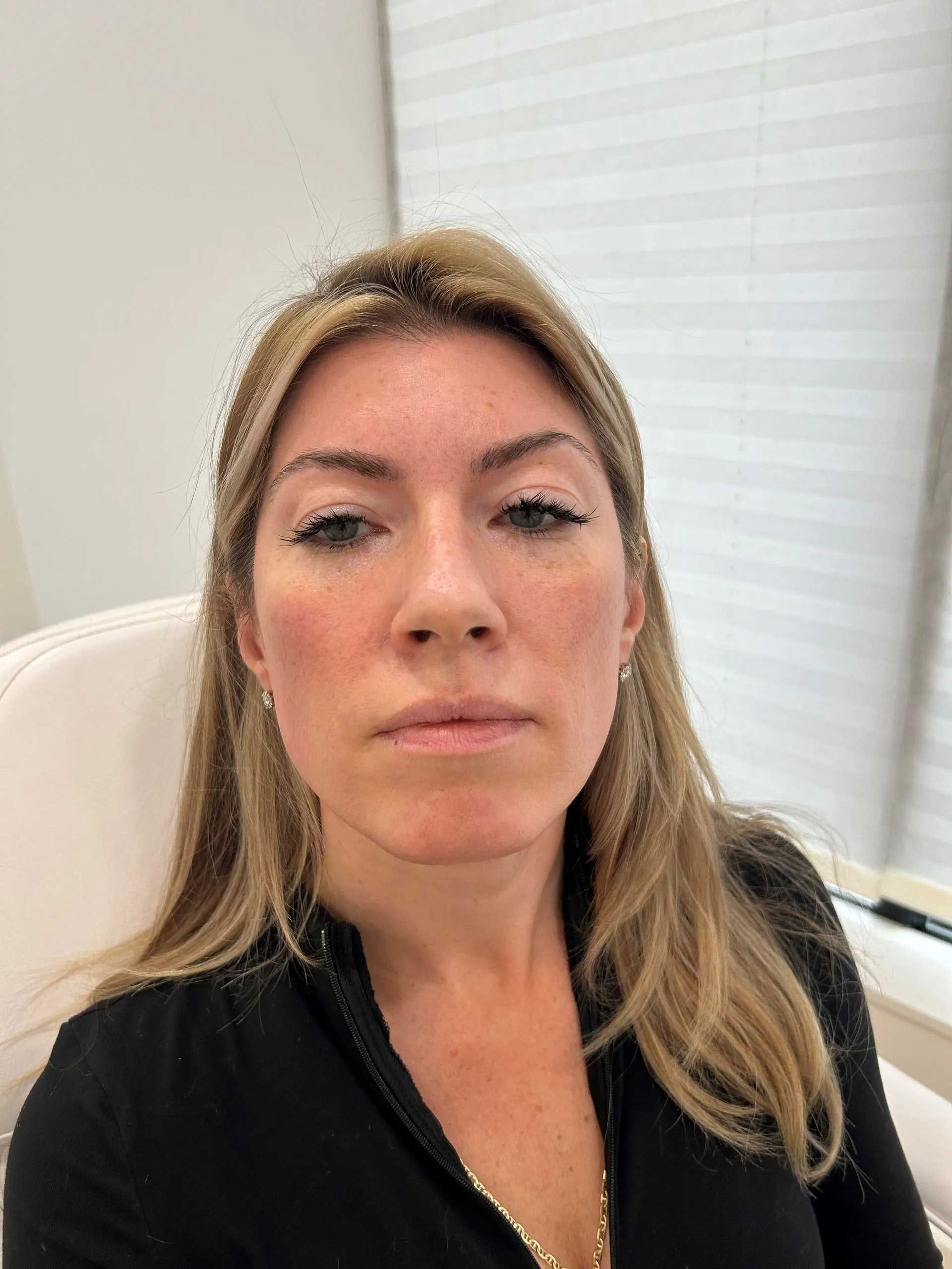 Woman with blonde hair in a black top, seated indoors. Light skin and subtle makeup.