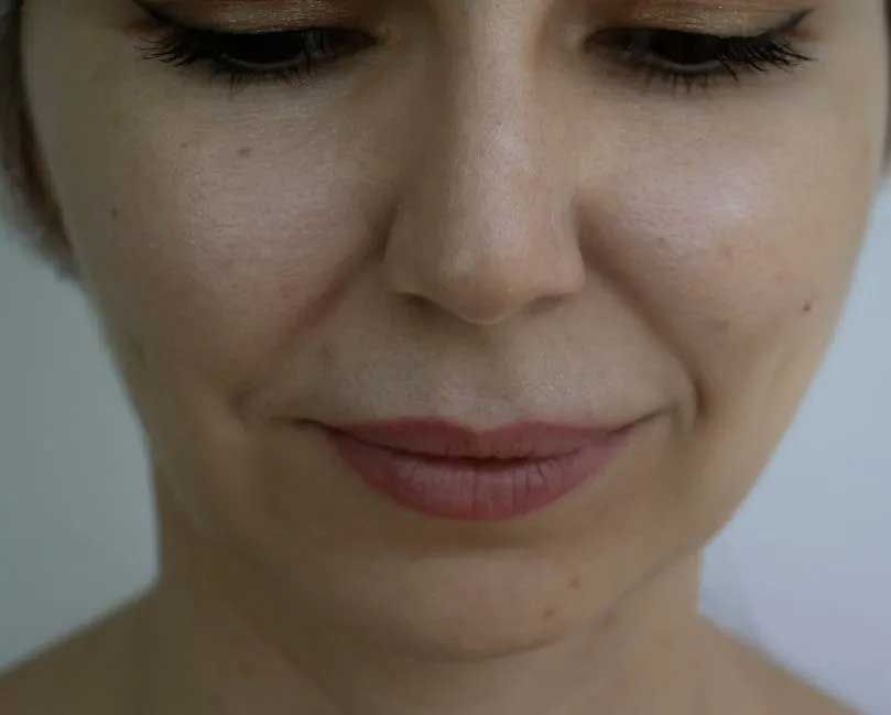 Close-up of a woman's face, looking down. Light skin with subtle makeup, neutral expression.