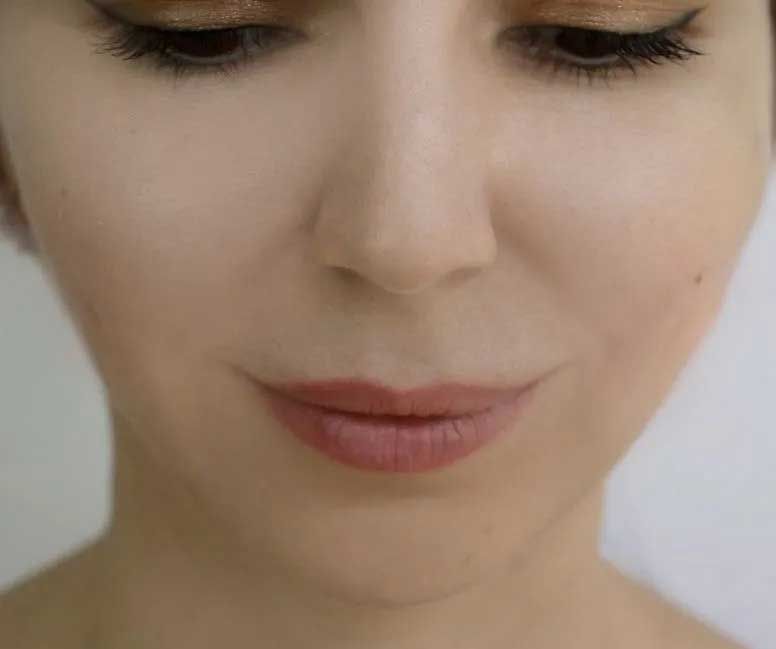 Close-up of a woman's face, looking down, with neutral makeup. Light skin, soft blush, and nude lipstick.