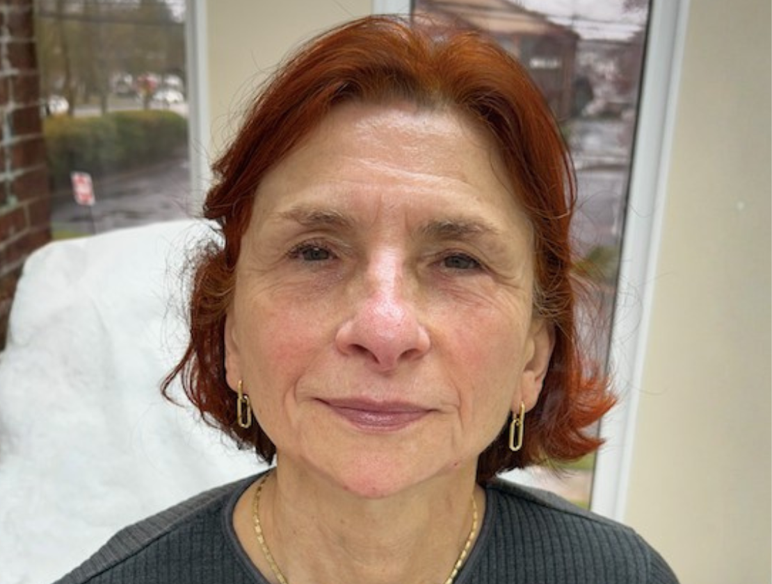 Woman with auburn hair and gold jewelry, indoors.