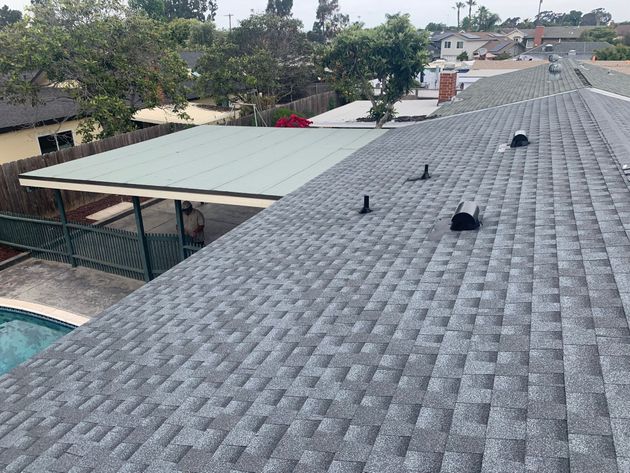 Rooftop with gray shingles, rooftop vents, and a view of nearby trees and houses
