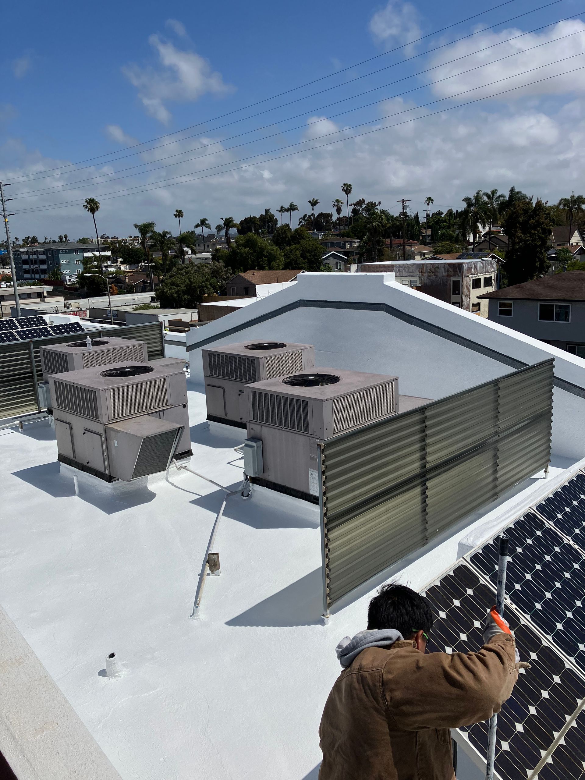 Person on a white rooftop near HVAC units and vents under a cloudy sky.