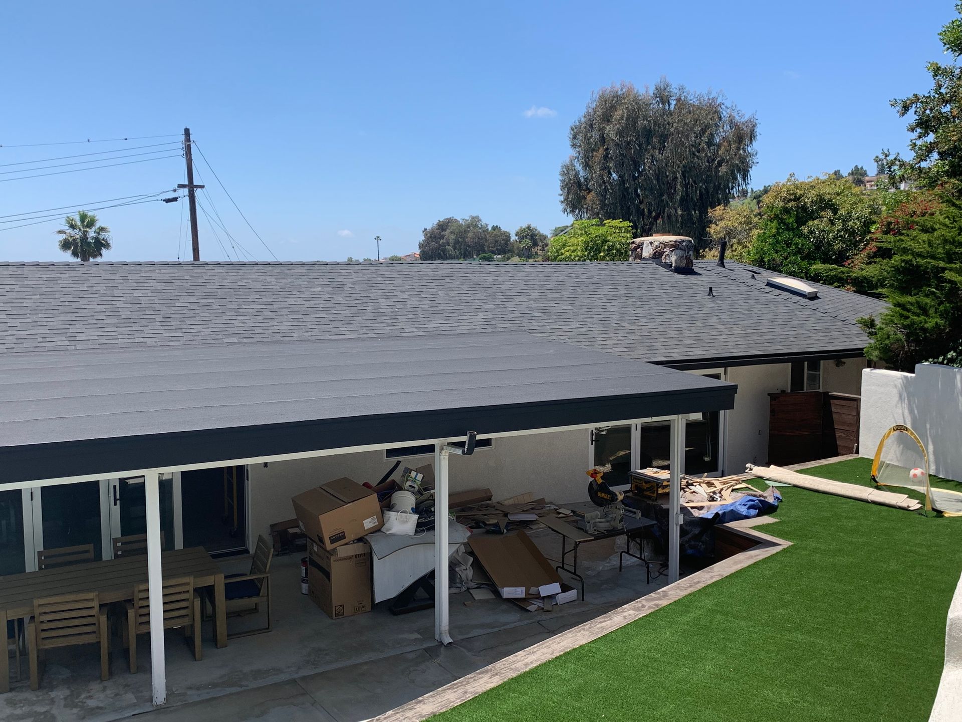 Backyard patio with a gray roof, covered seating area, and green lawn under a clear blue sky