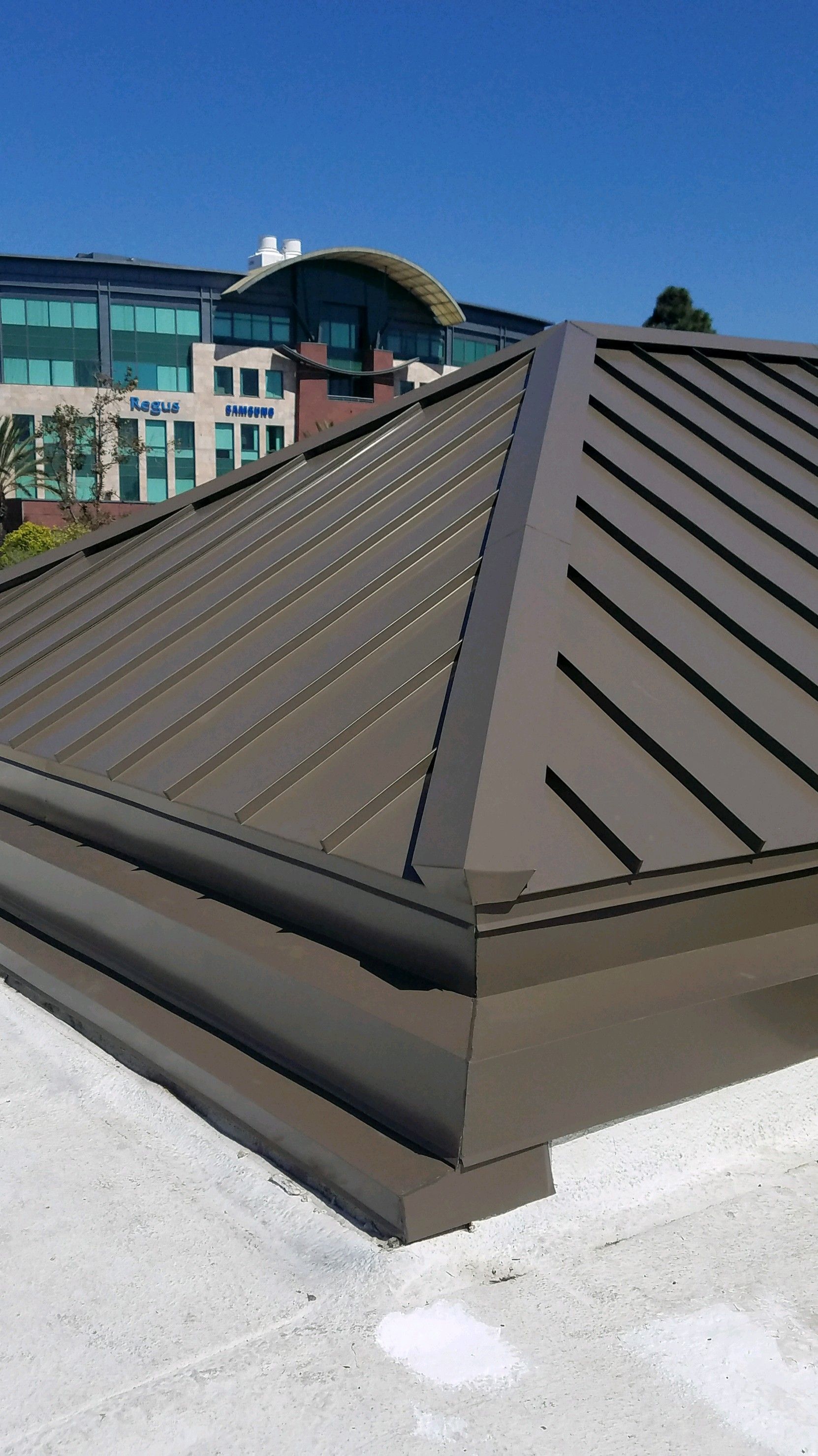 Brown metal roof on a building with a white rooftop and a glass office building in the background