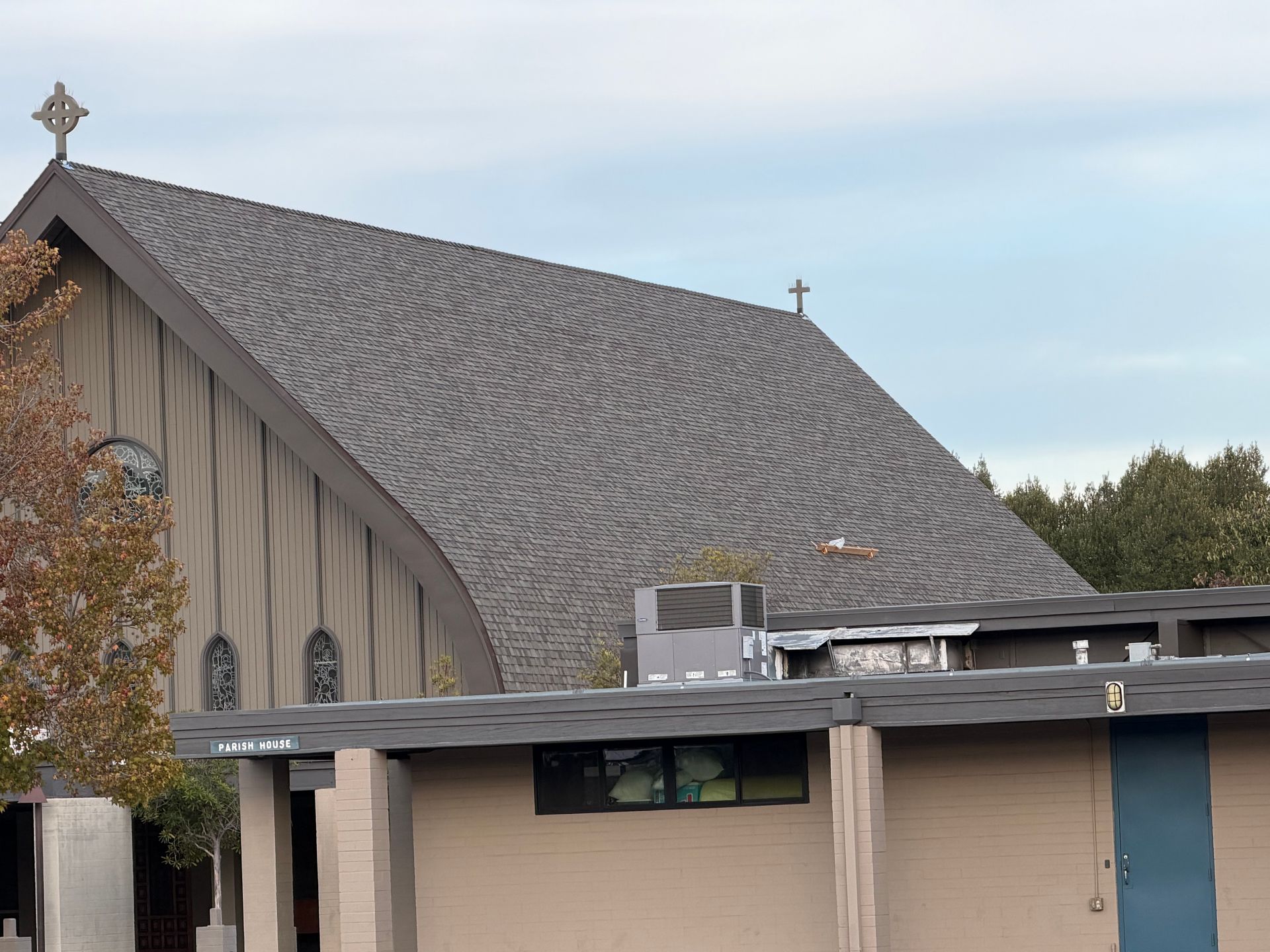 Church building with gray shingled roof and beige walls under a blue sky