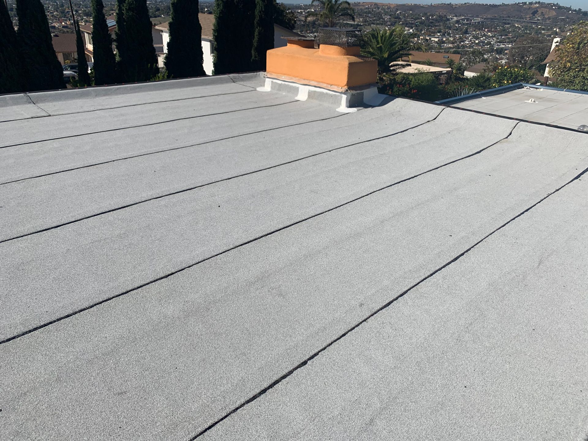 Flat white roof with an orange vent chimney, overlooking a hillside neighborhood.