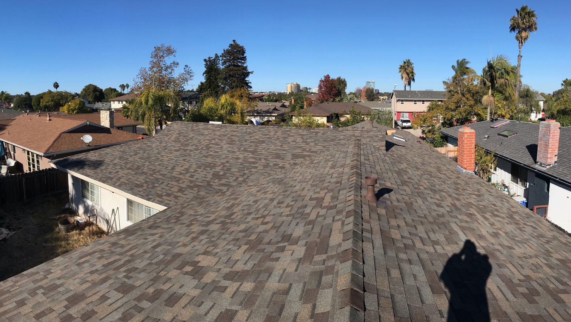 Wide view of a shingled rooftop in a residential neighborhood on a sunny day