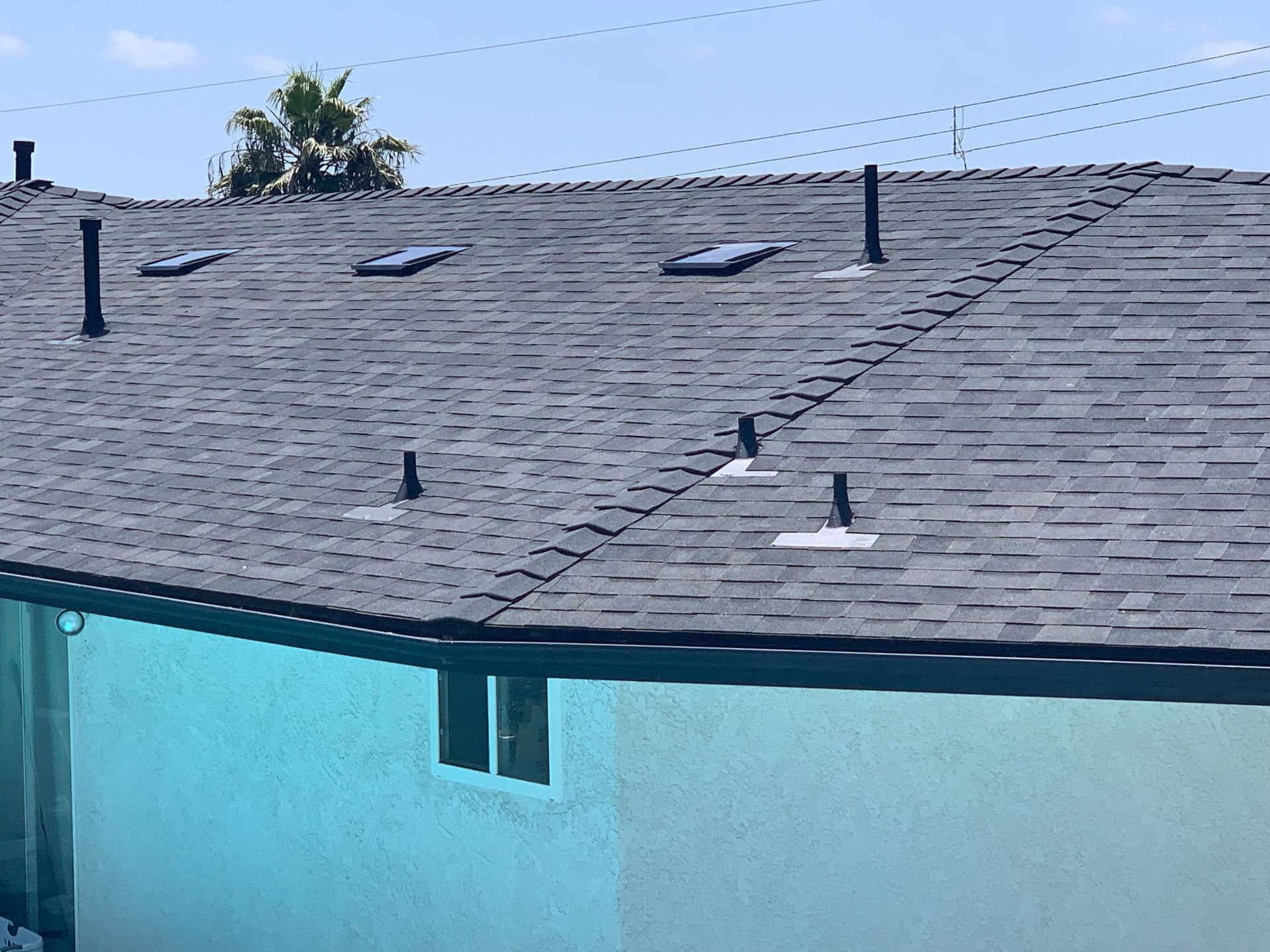 Blue house roof with gray shingles and several vents under a clear sky