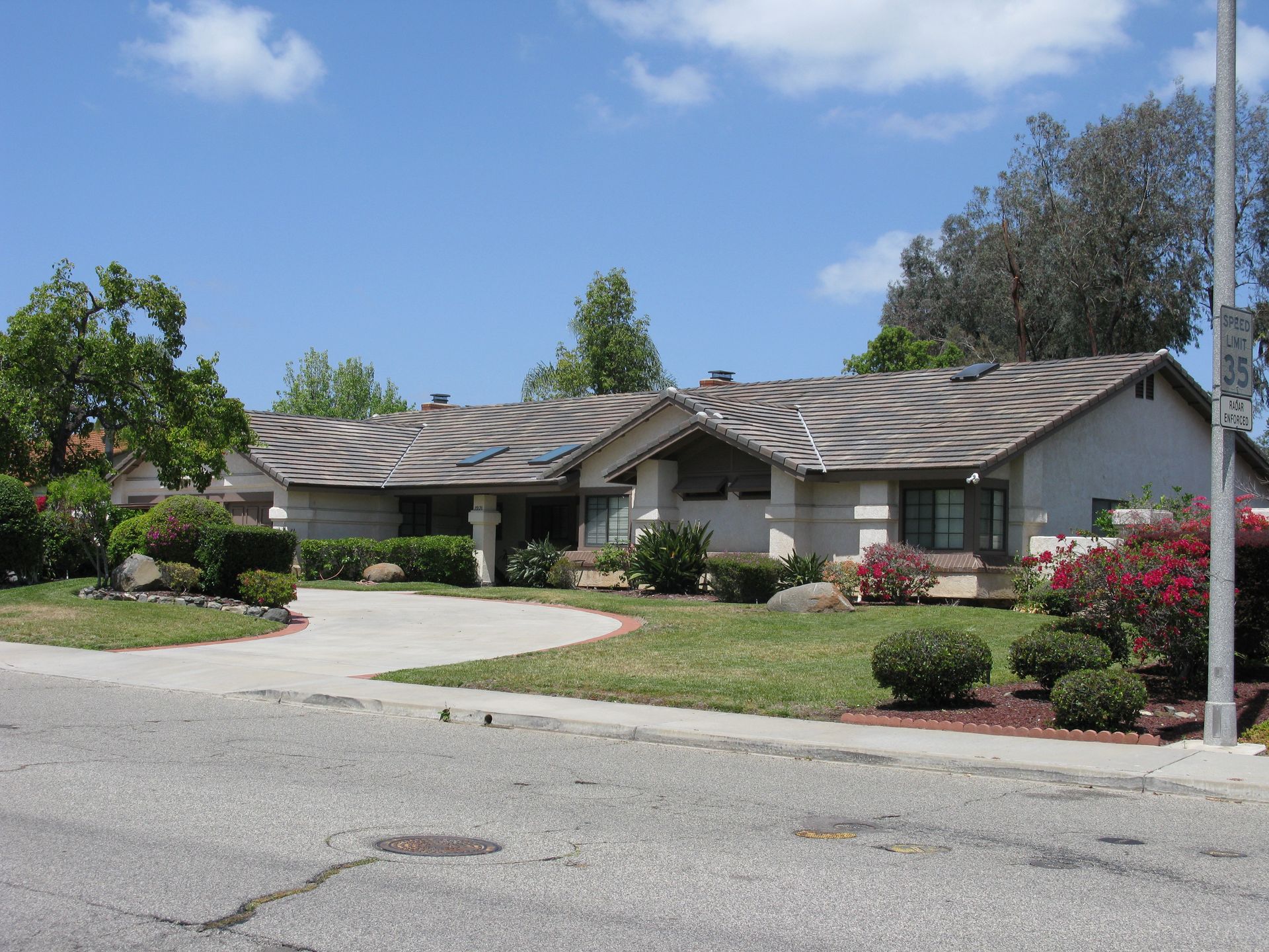 Single-story suburban house with a tiled roof, landscaped front yard, and curved driveway on a sunny day