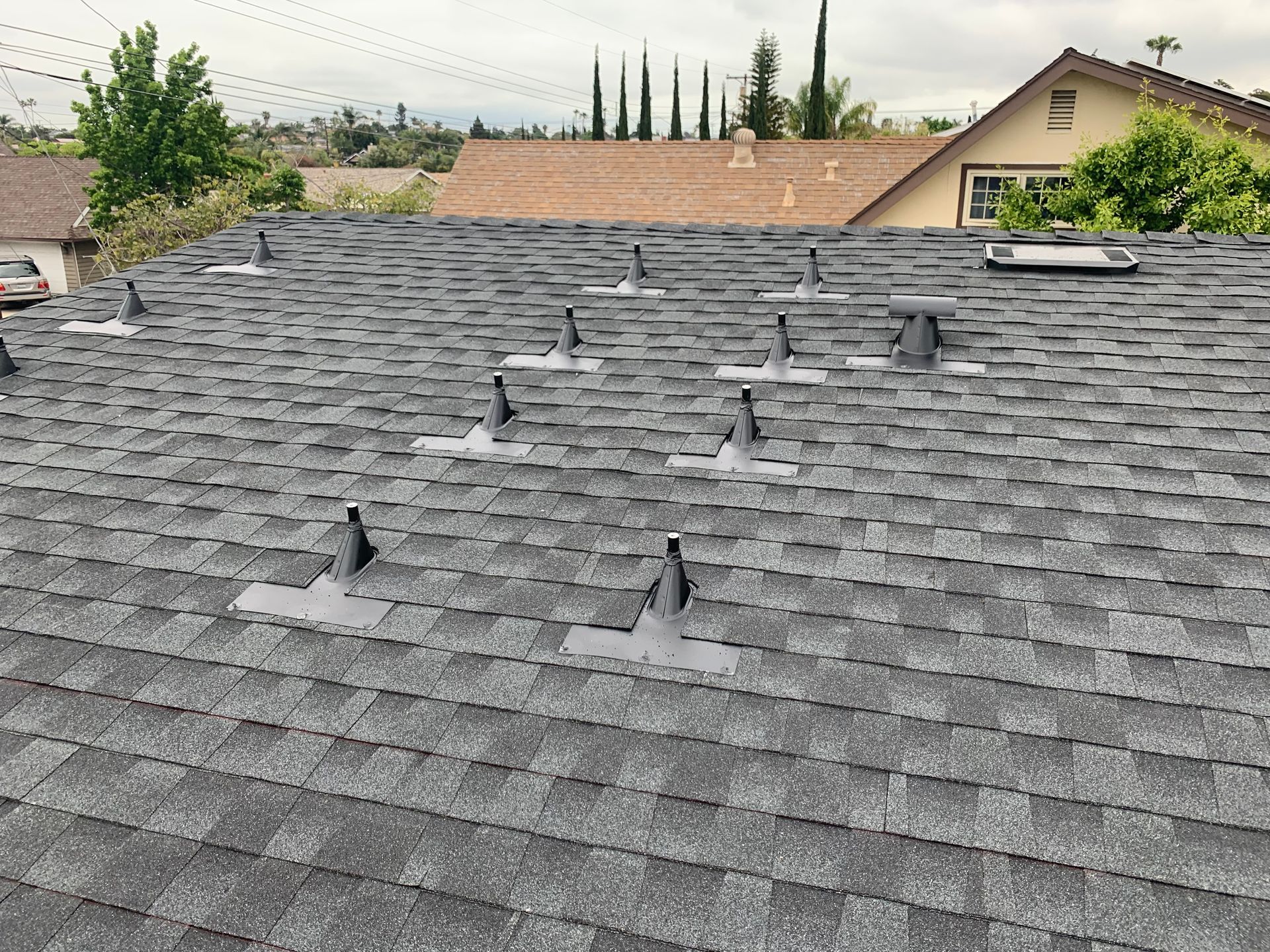 Gray shingled roof with several black vent pipes and rooftops visible in the background
