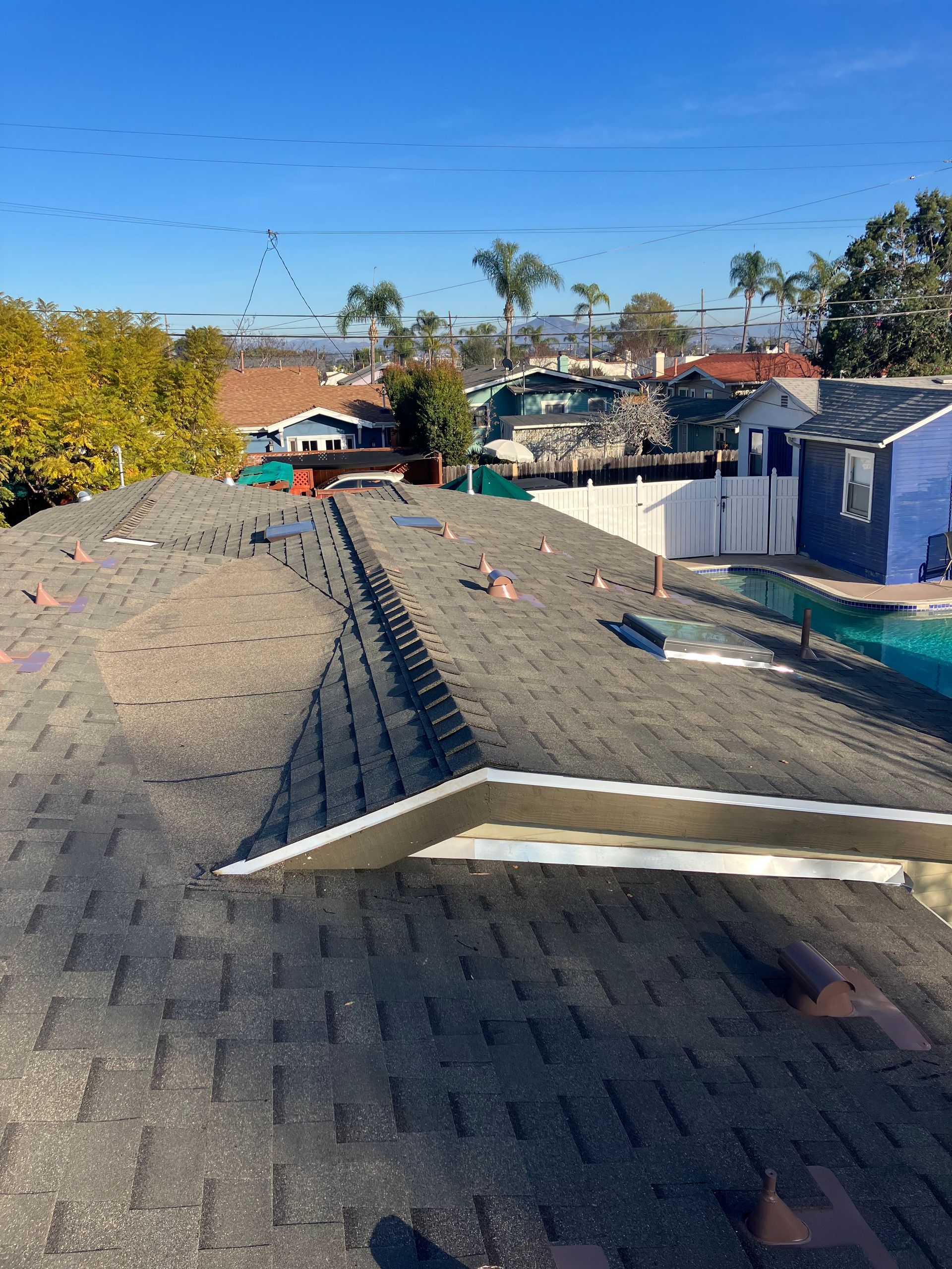 Rooftop with damaged shingles, scattered debris, and a partially detached roof edge under a clear blue sky
