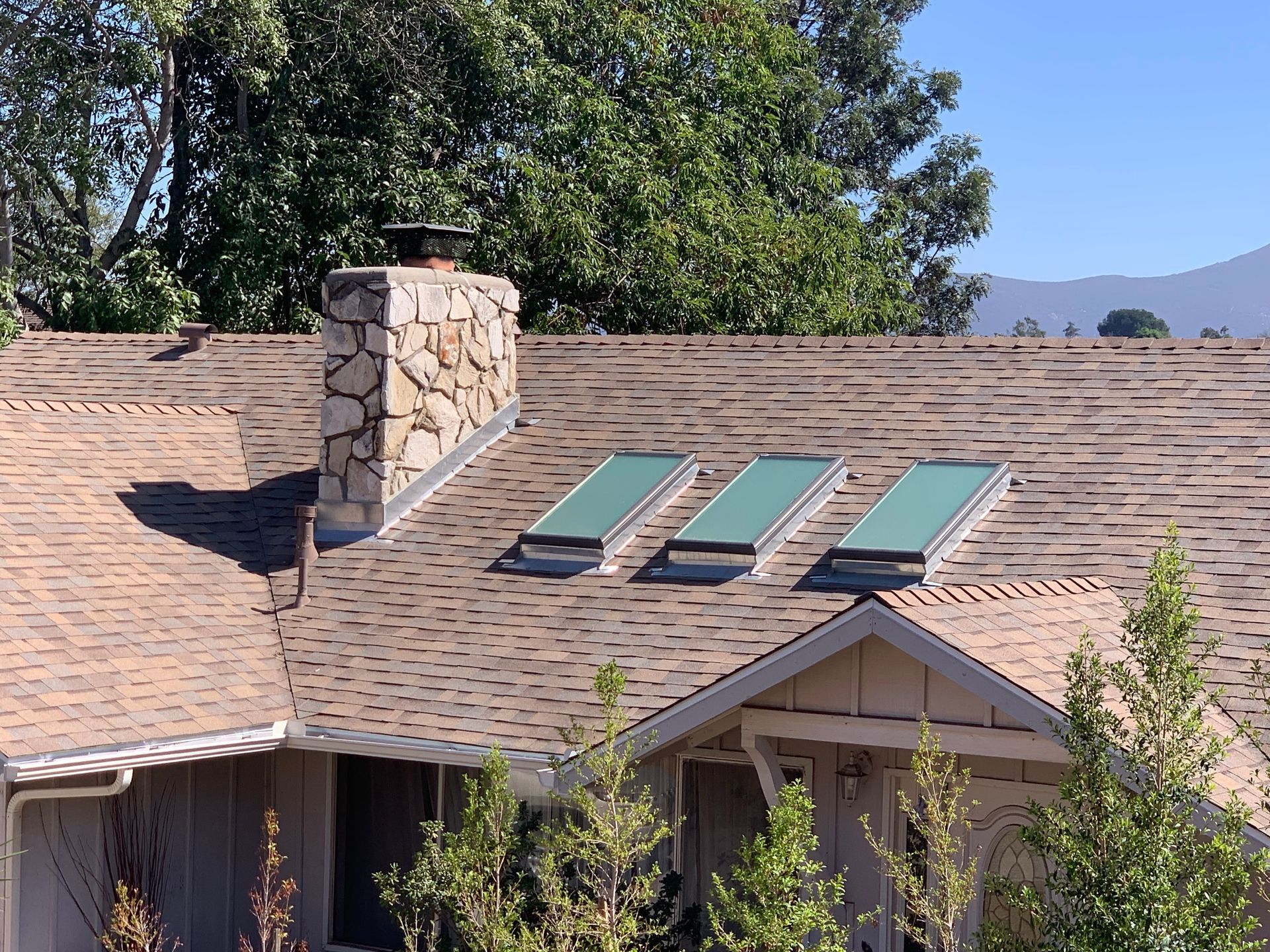 House roof with stone chimney and three skylights under a clear blue sky.
