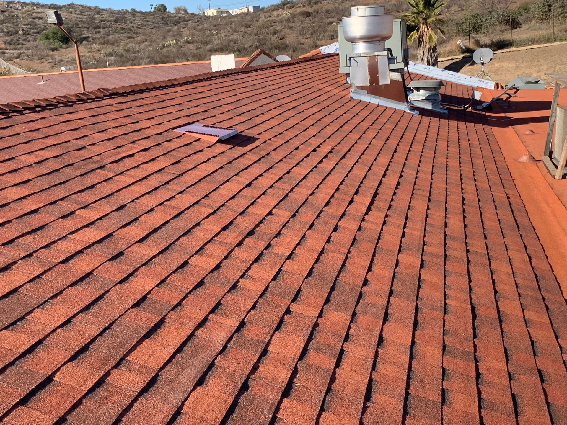 Red tiled rooftop with solar panels and rooftop vents in a dry hillside setting