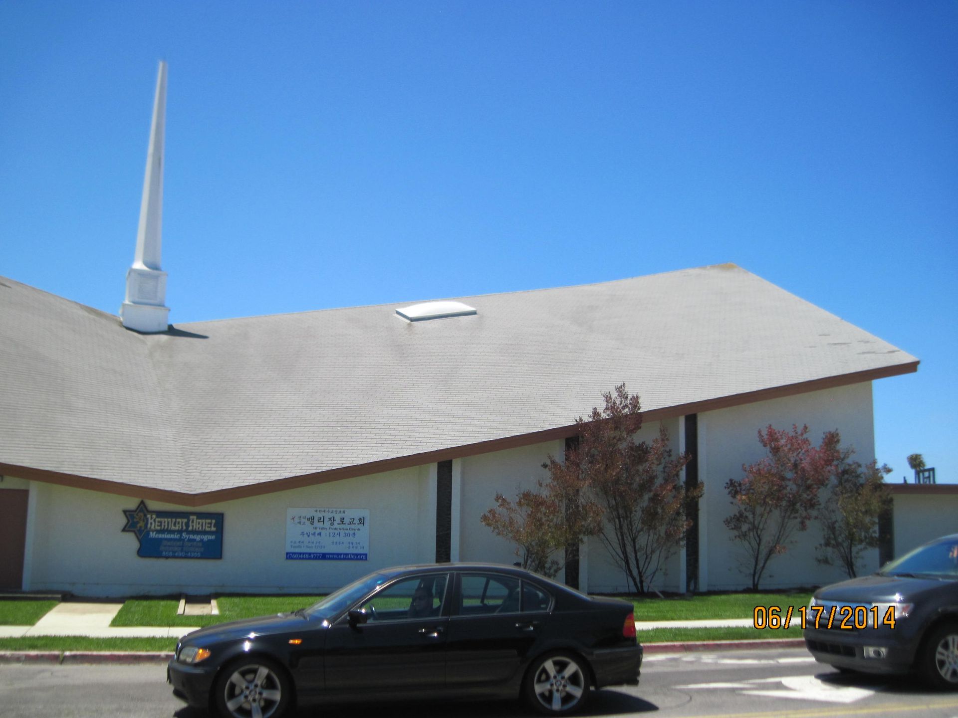 Church building with a white roof, blue sky, and cars parked in front