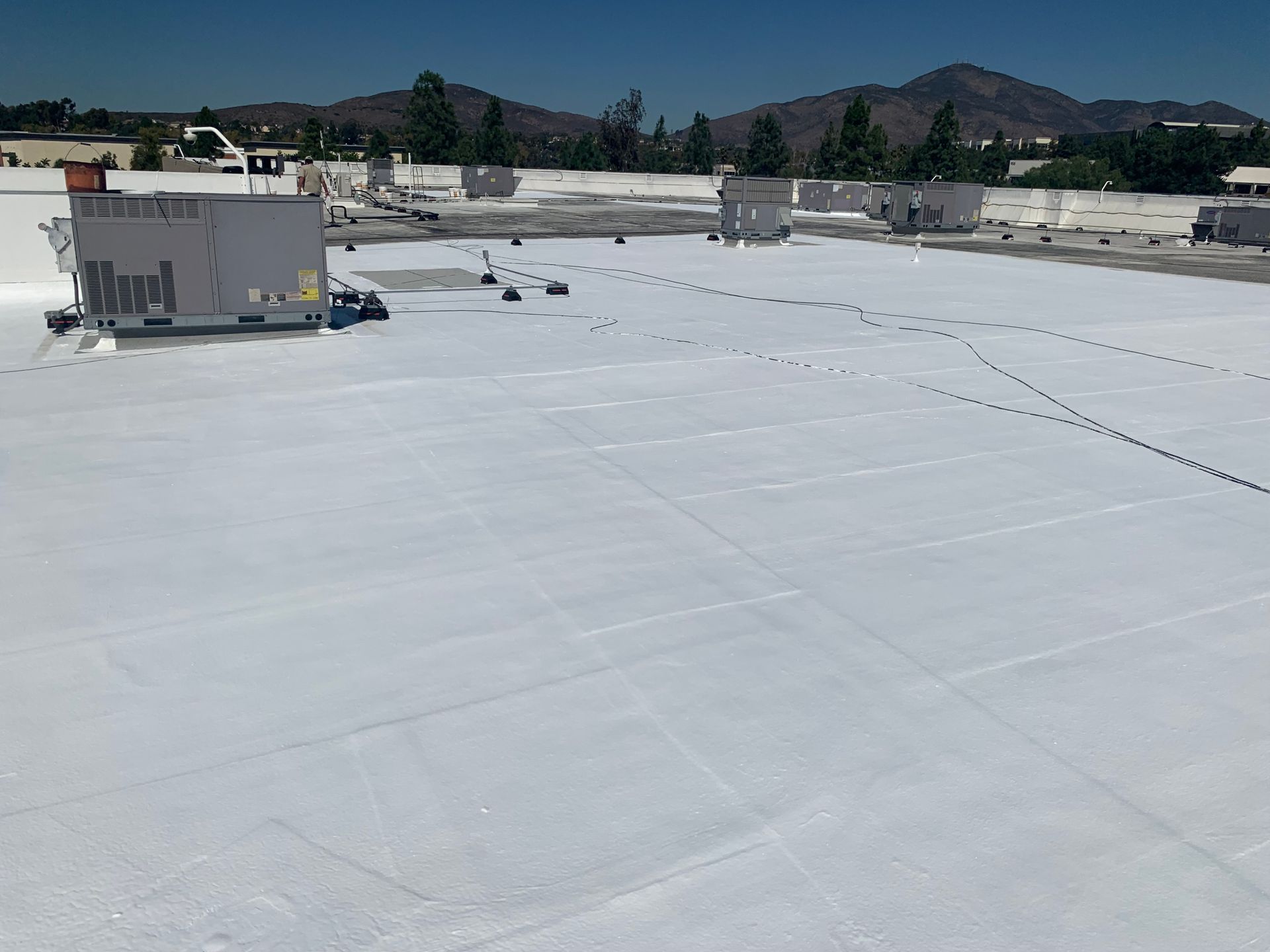 White flat rooftop with HVAC units and distant mountains under a clear blue sky