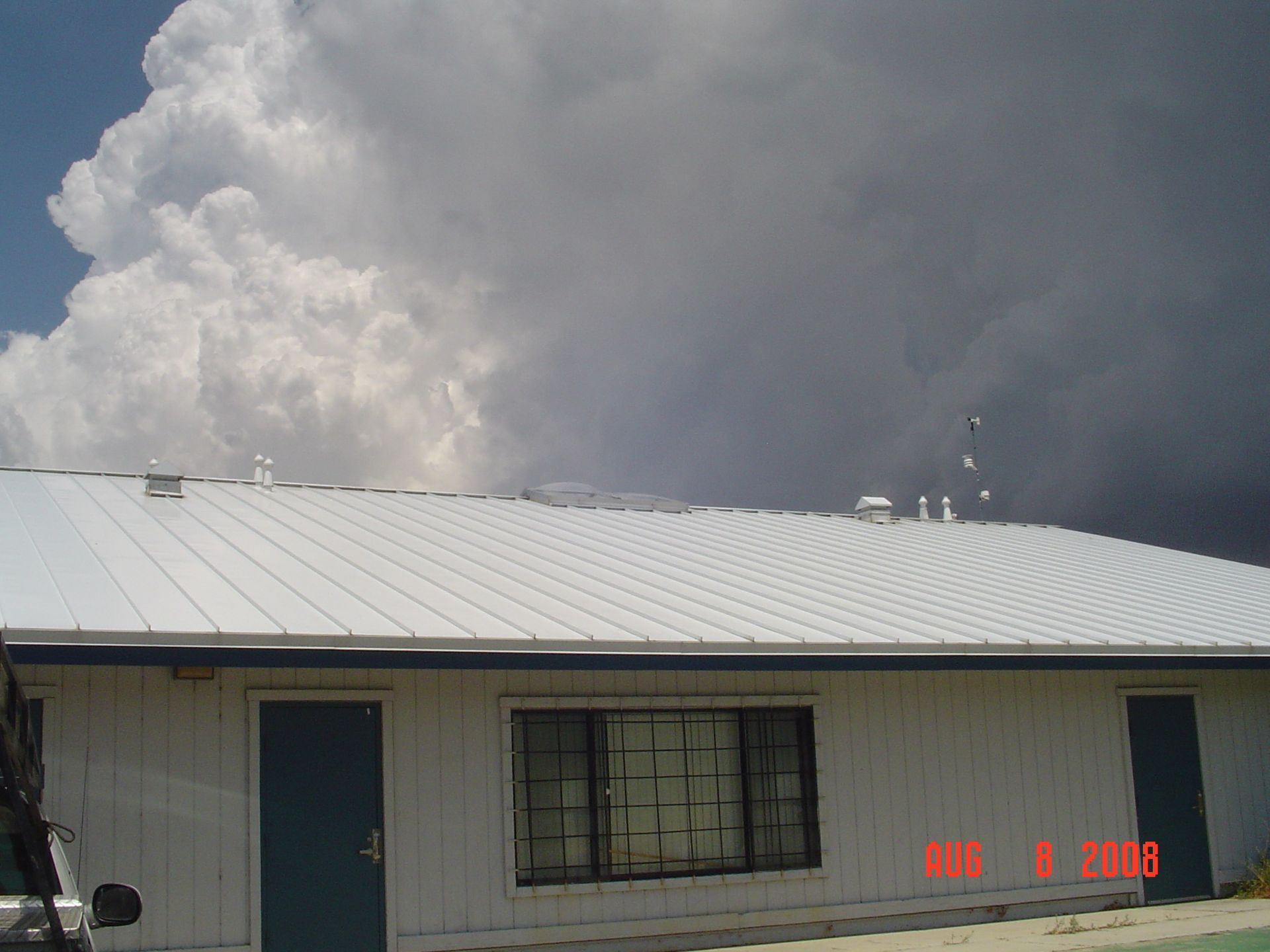 Small white building with a blue door under a large gray cloud in the sky
