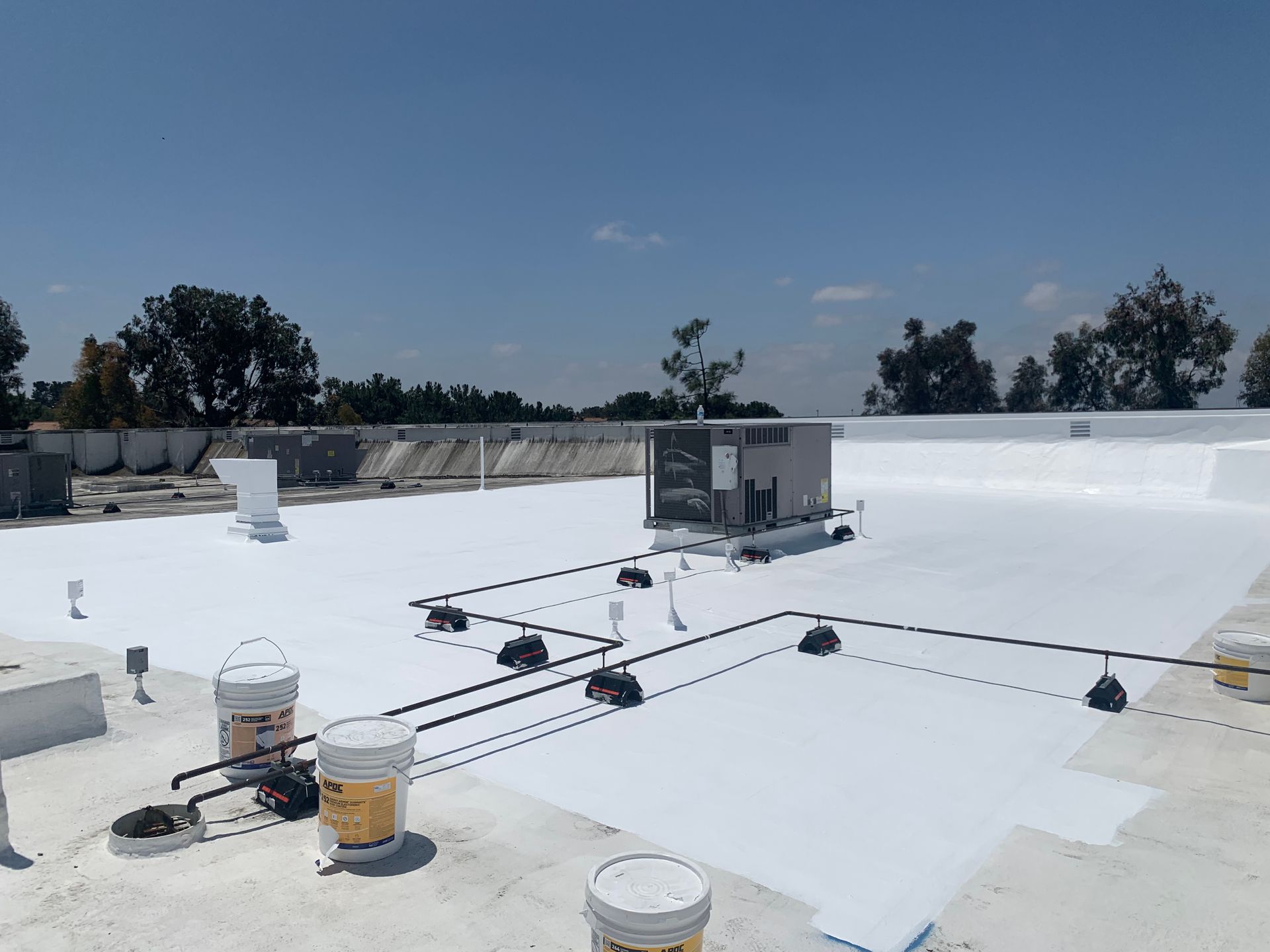 White flat roof with HVAC units, vents, and pipes under a clear blue sky.