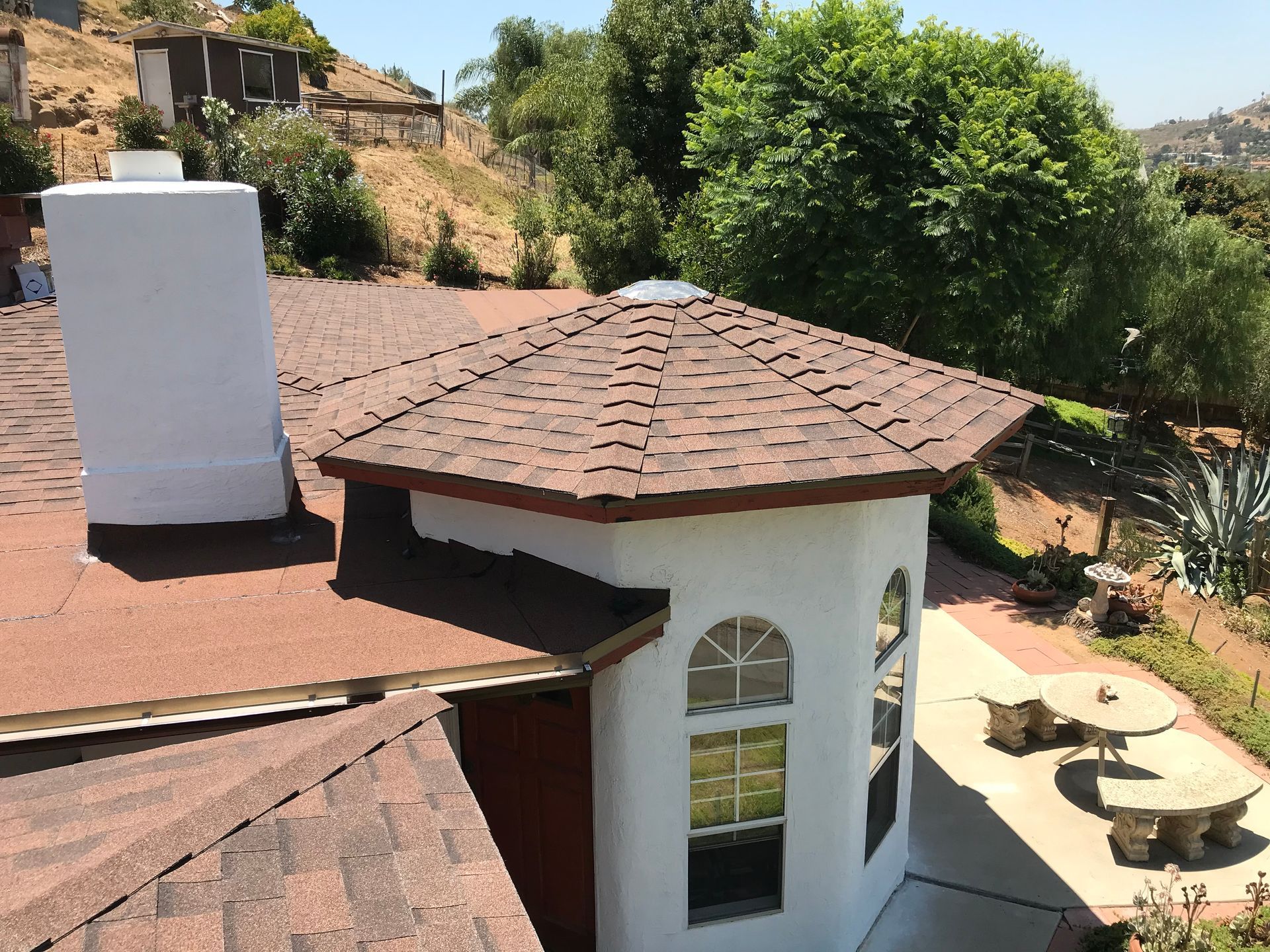 Patio with a red-tile roof gazebo beside a house, overlooking a hillside yard with trees and a picnic table