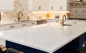 Modern white kitchen with a large island, gold fixtures, and blue patterned backsplash