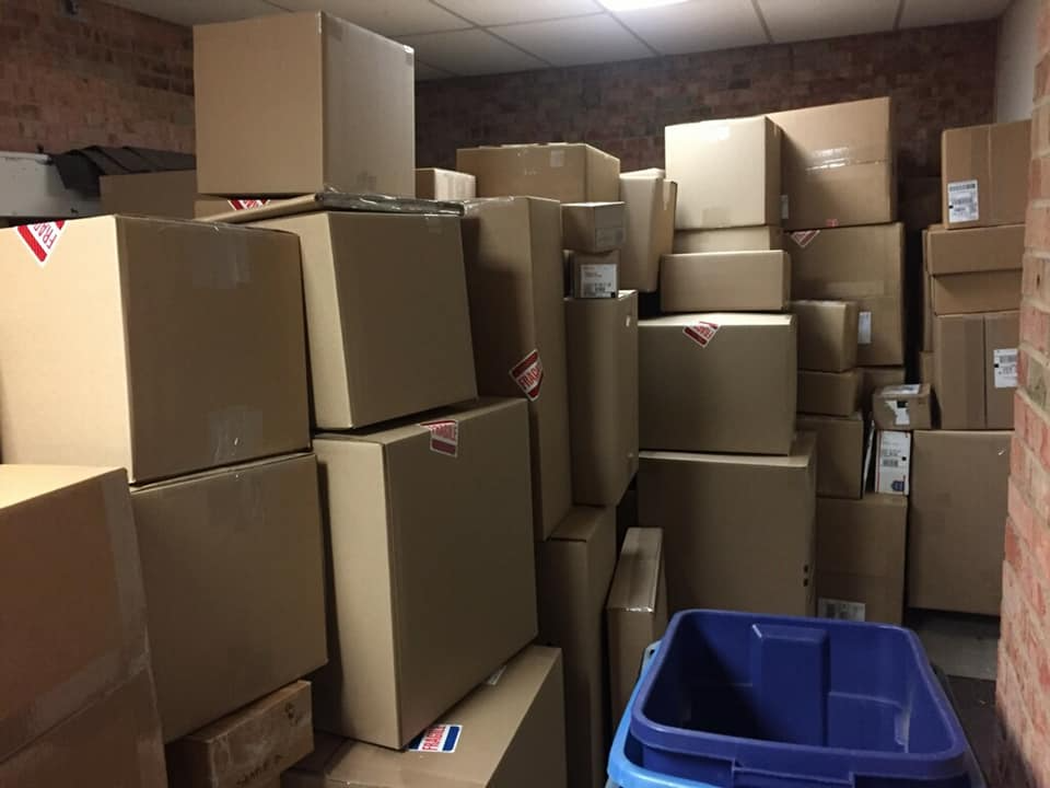 A cluttered storage room filled with many brown cardboard boxes. A blue bin is in the foreground.
