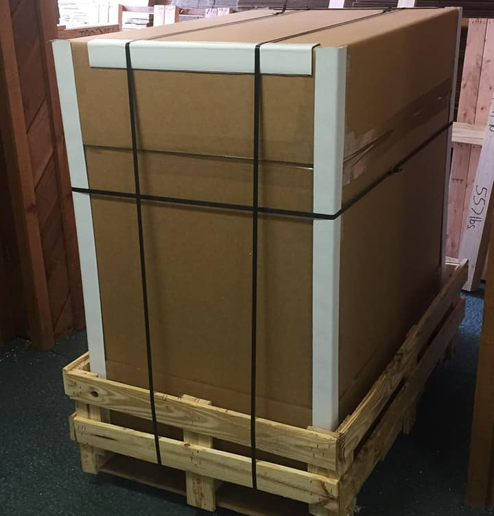 Large cardboard box secured with straps, sitting on a wooden pallet.