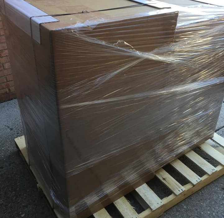 Large, cardboard box wrapped in clear plastic on a wooden pallet, outdoors.