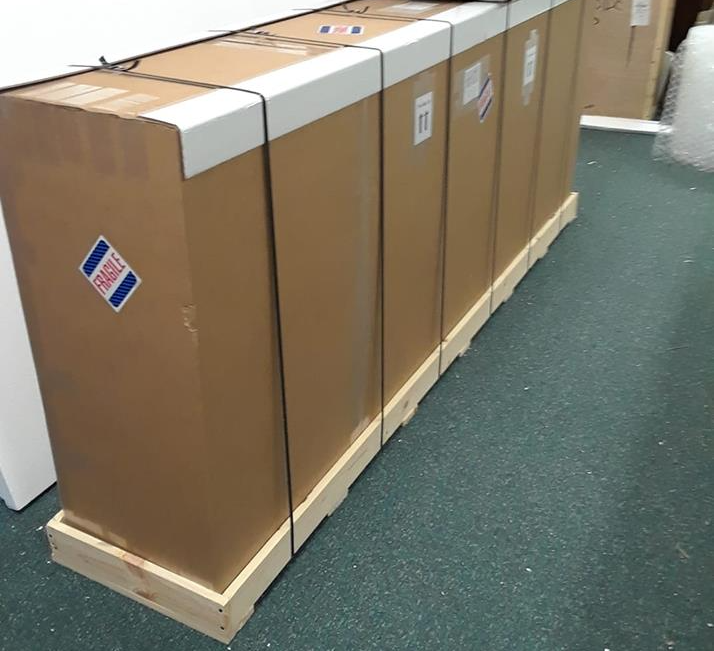 Boxes secured with bands on wooden pallet, indoors on green carpet.