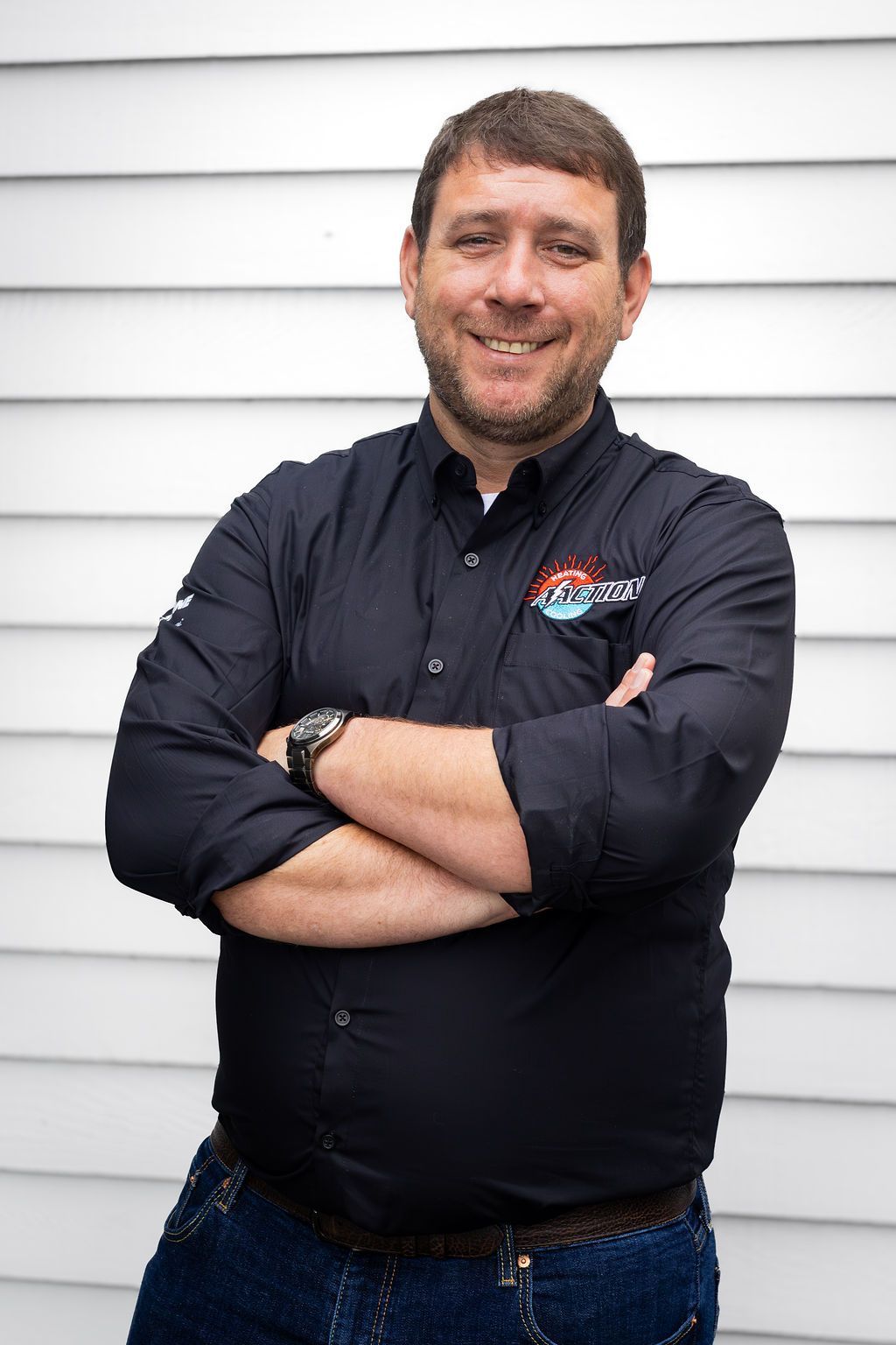 Smiling man with crossed arms in a black shirt standing against white siding.
