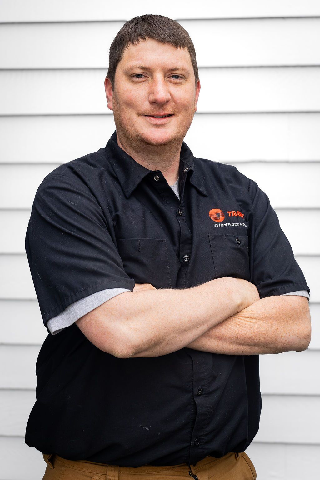 Person in black shirt with arms crossed, standing in front of white siding.