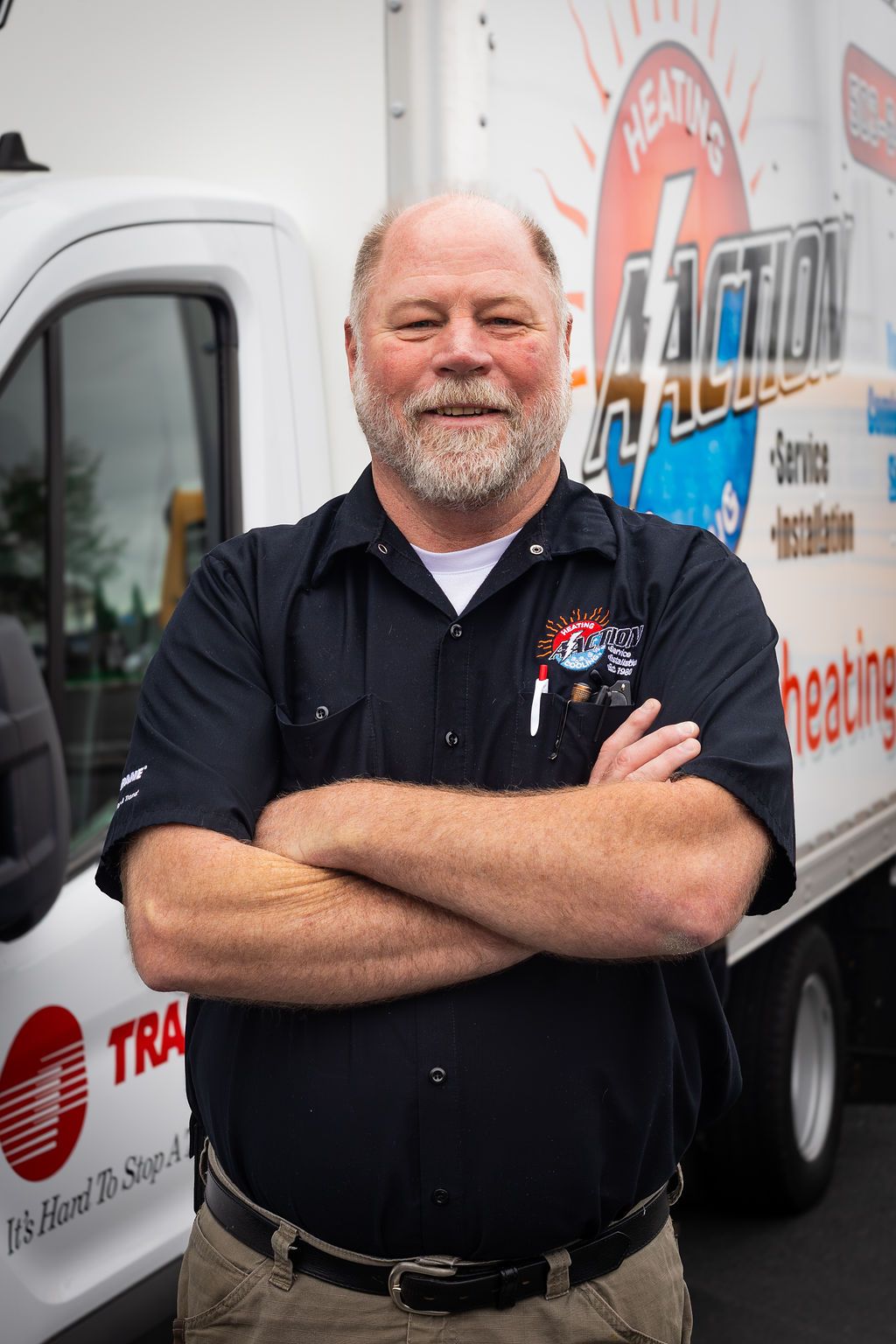 Man standing with arms crossed beside a branded truck, wearing a black shirt and smiling.