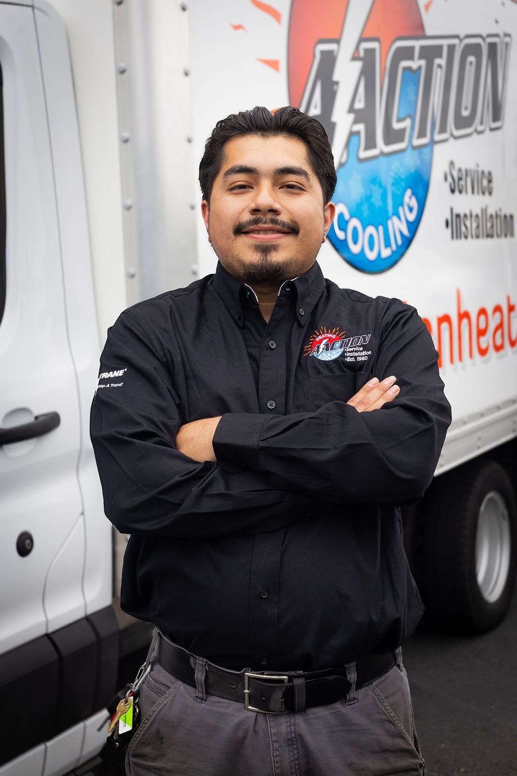Person in black jacket standing with arms crossed beside a white service van.