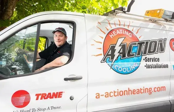 A technician sits in the driver’s seat of a white A-Action Heating and Cooling service van featuring the Trane logo.