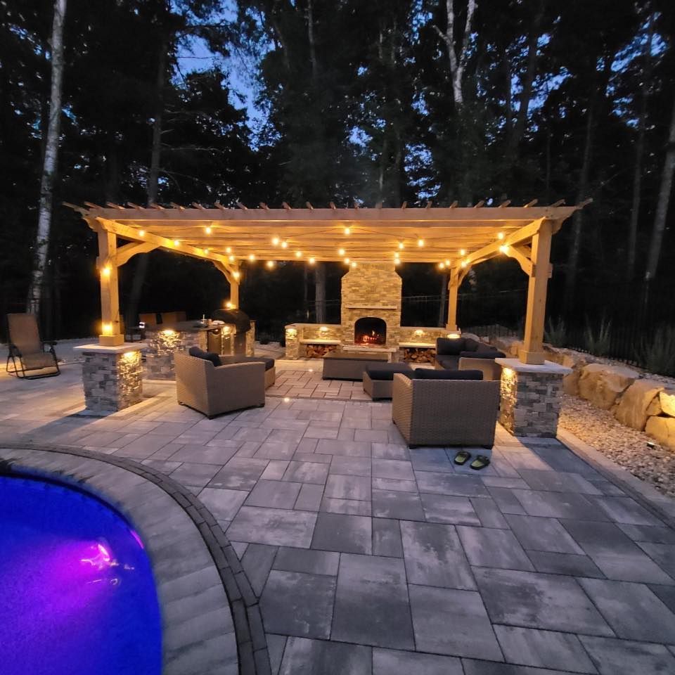 A patio with a pergola and a fireplace at night