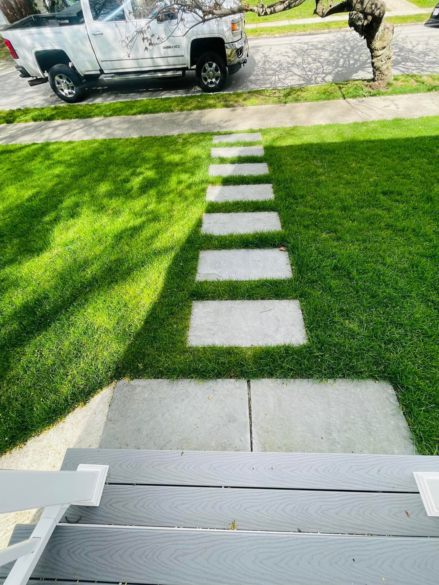 A white truck is parked in the grass next to a stone walkway.