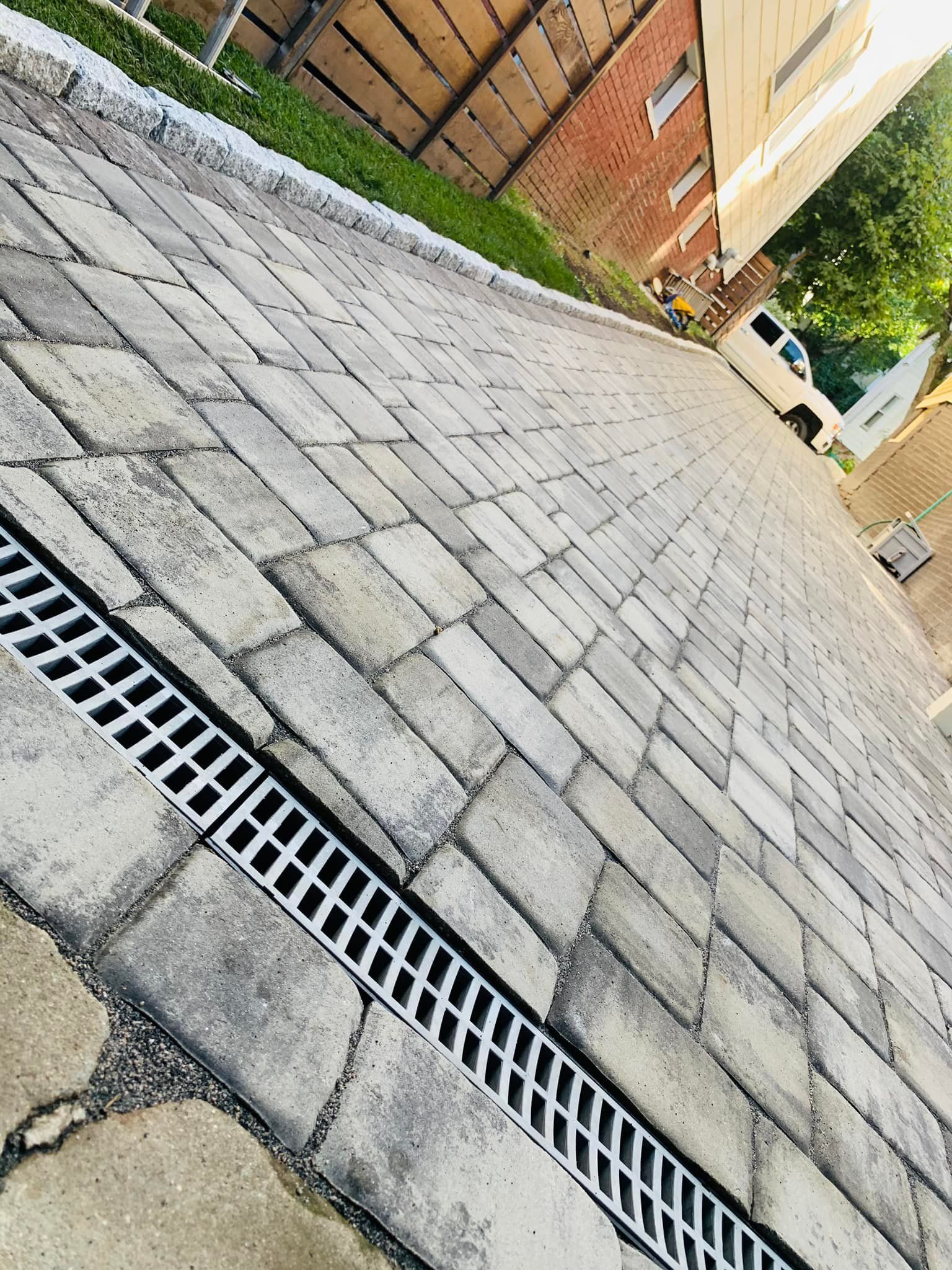 A drain on a brick driveway next to a building.